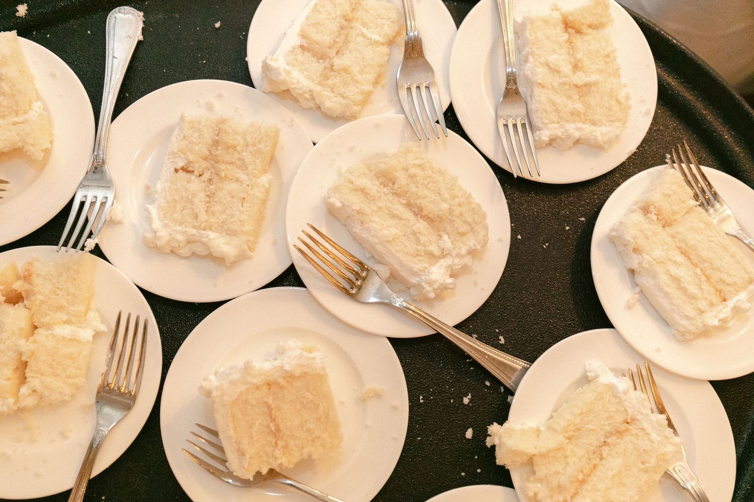 Multiple plates of white wedding cake served and ready for guests at the reception.