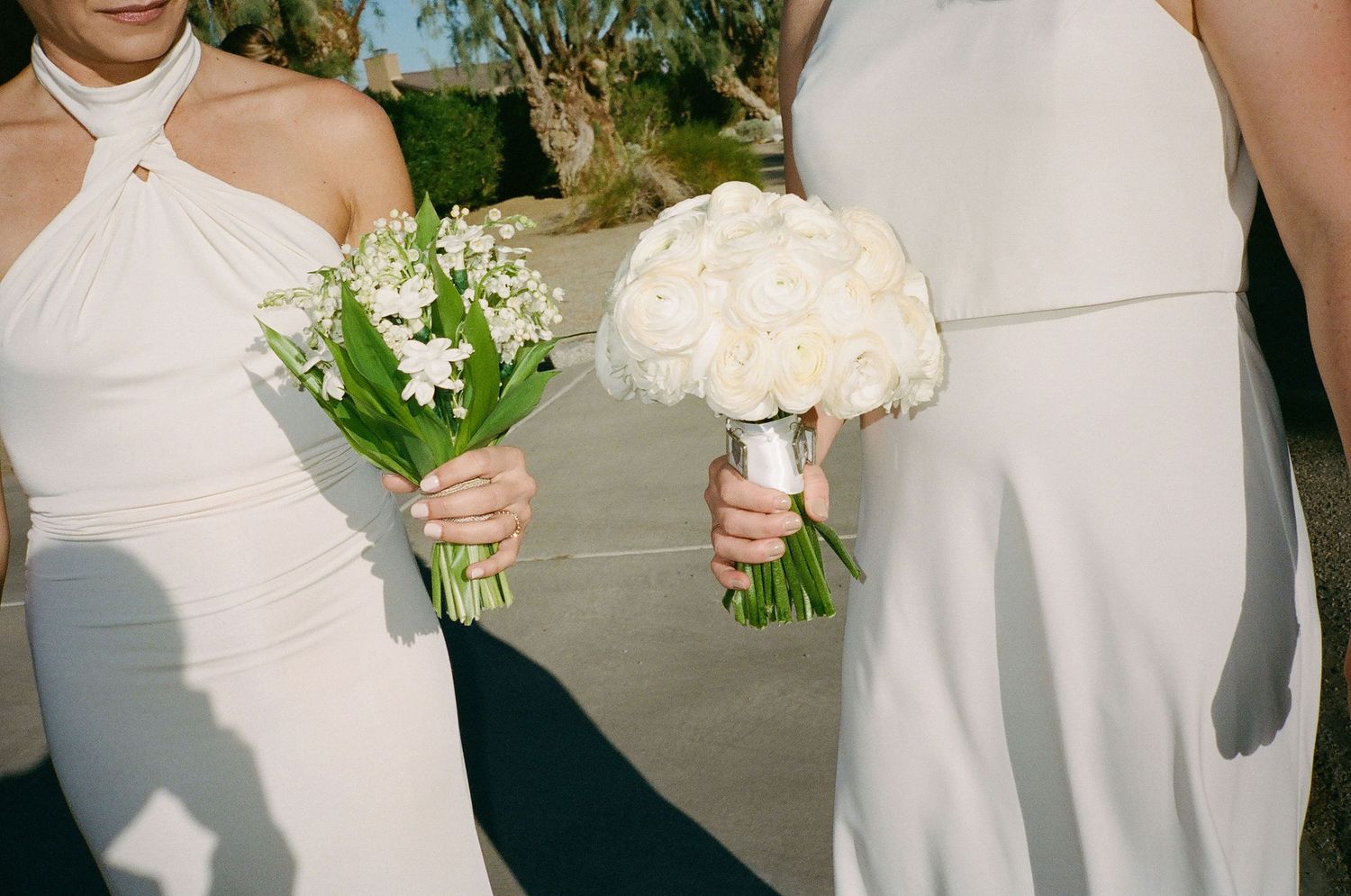 Wedding party members holding white floral bouquets in elegant white dresses.