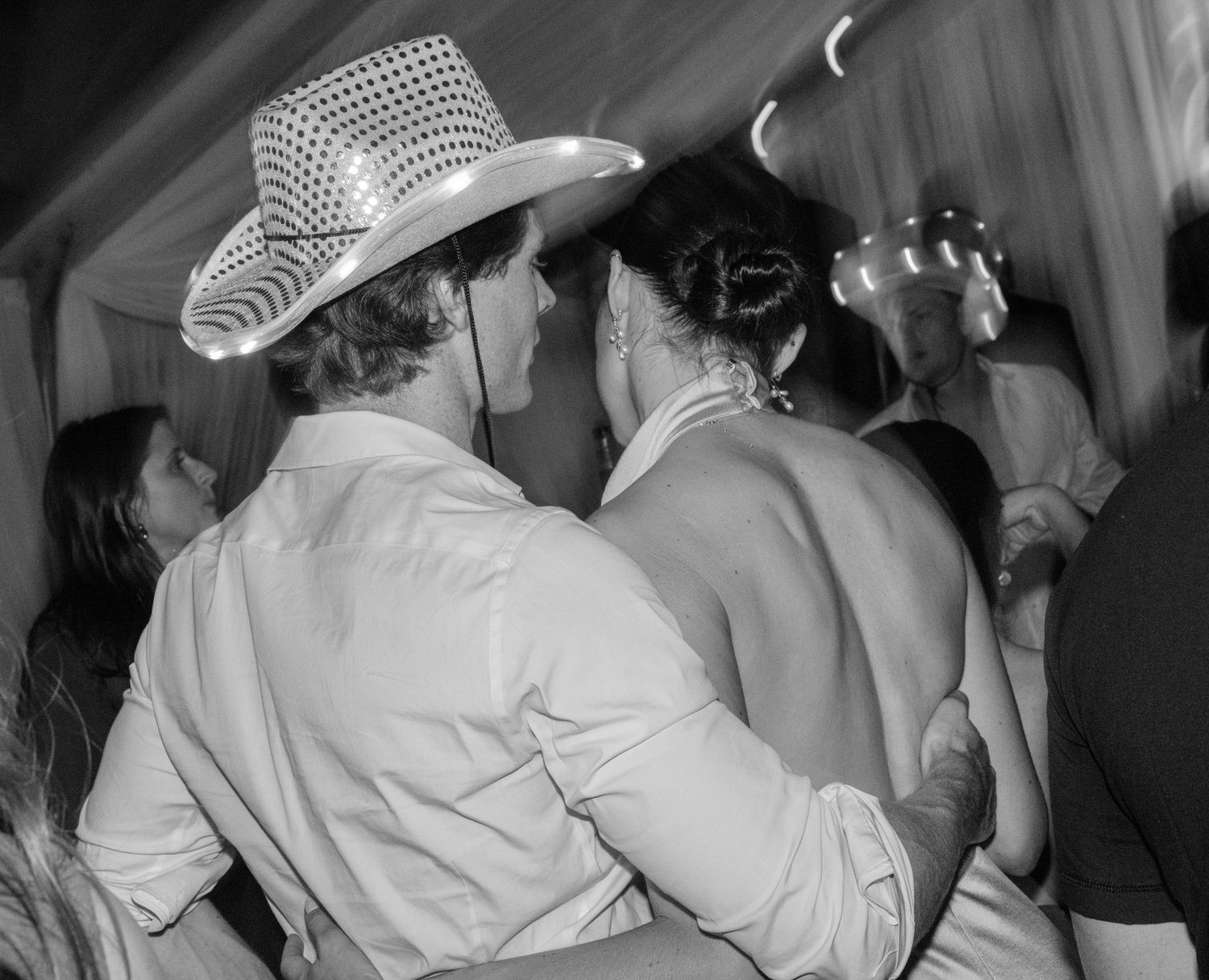 Black and white photo of guests dancing at a lively party wearing cowboy hats.