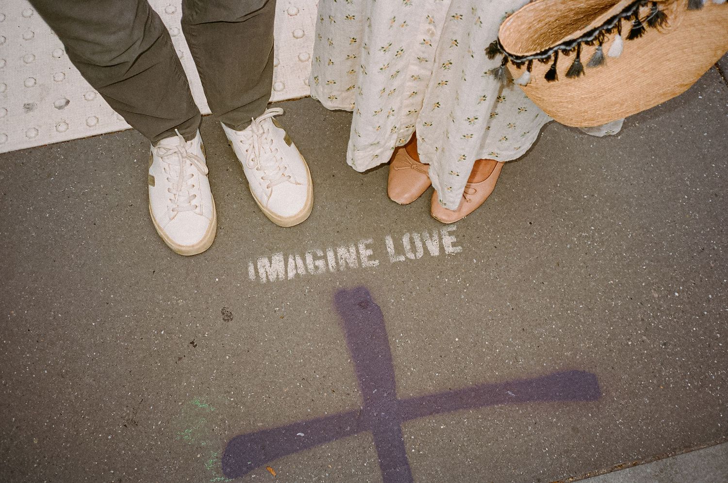 Couple standing over 'Imagine Love' pavement stencil, wearing white sneakers and boho wedding attire.