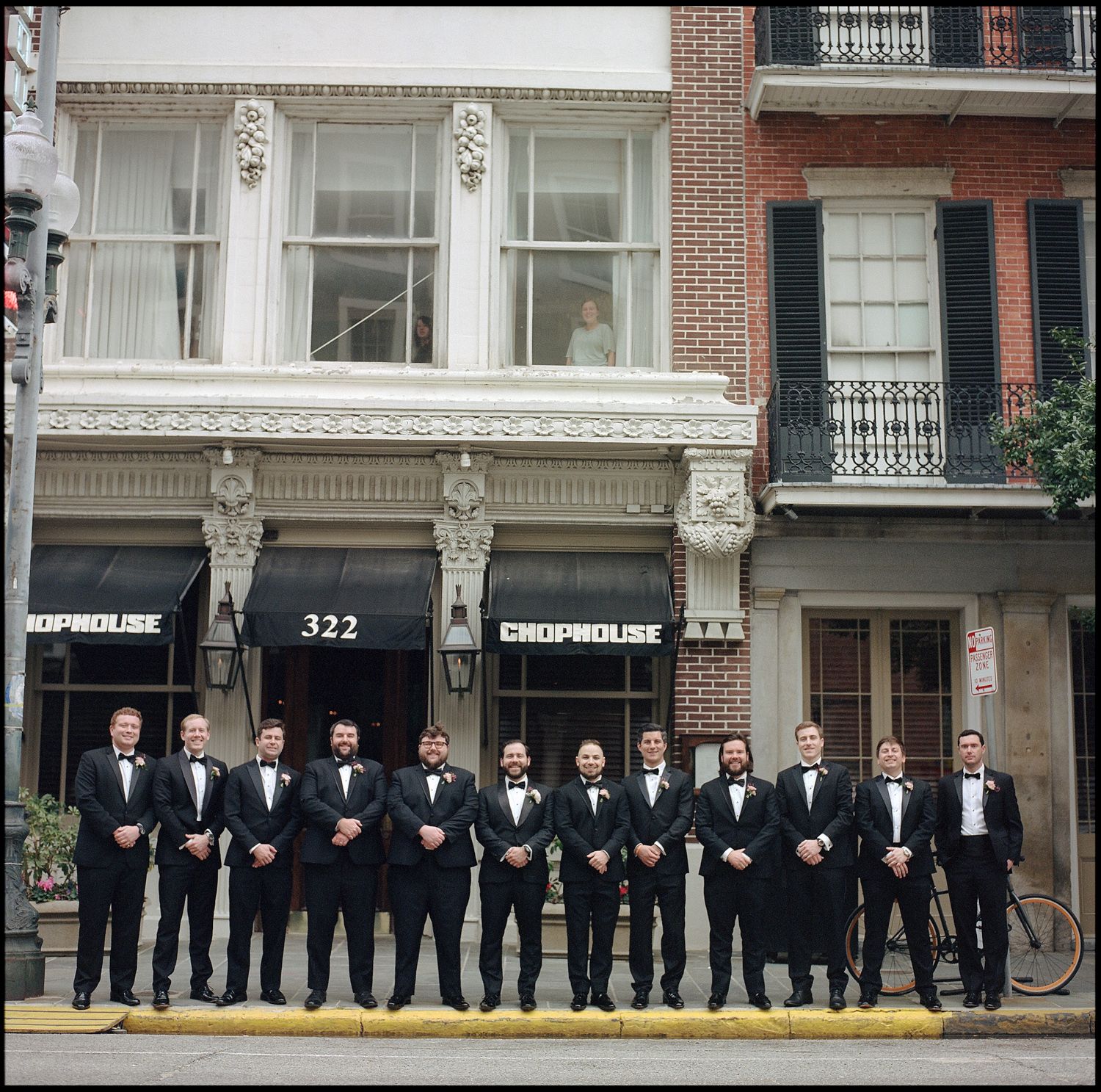 Groomsmen in black tuxedos lined up outside 322 Crophouse building for a wedding party photo.