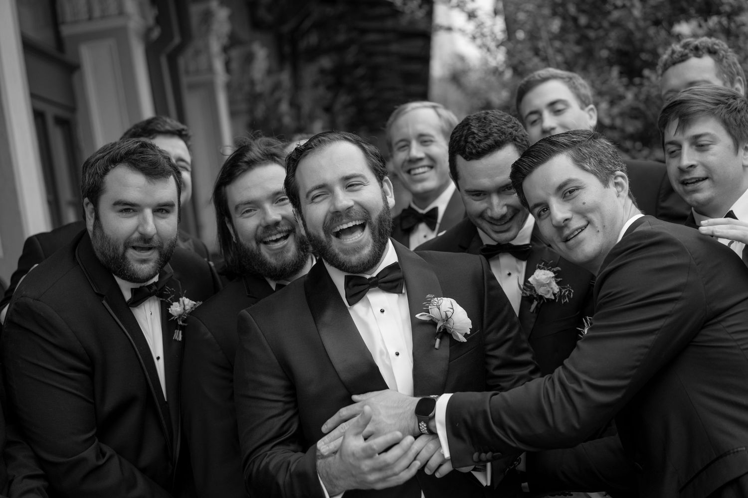 Groomsmen sharing laughs and embraces in formal wear during wedding photos.