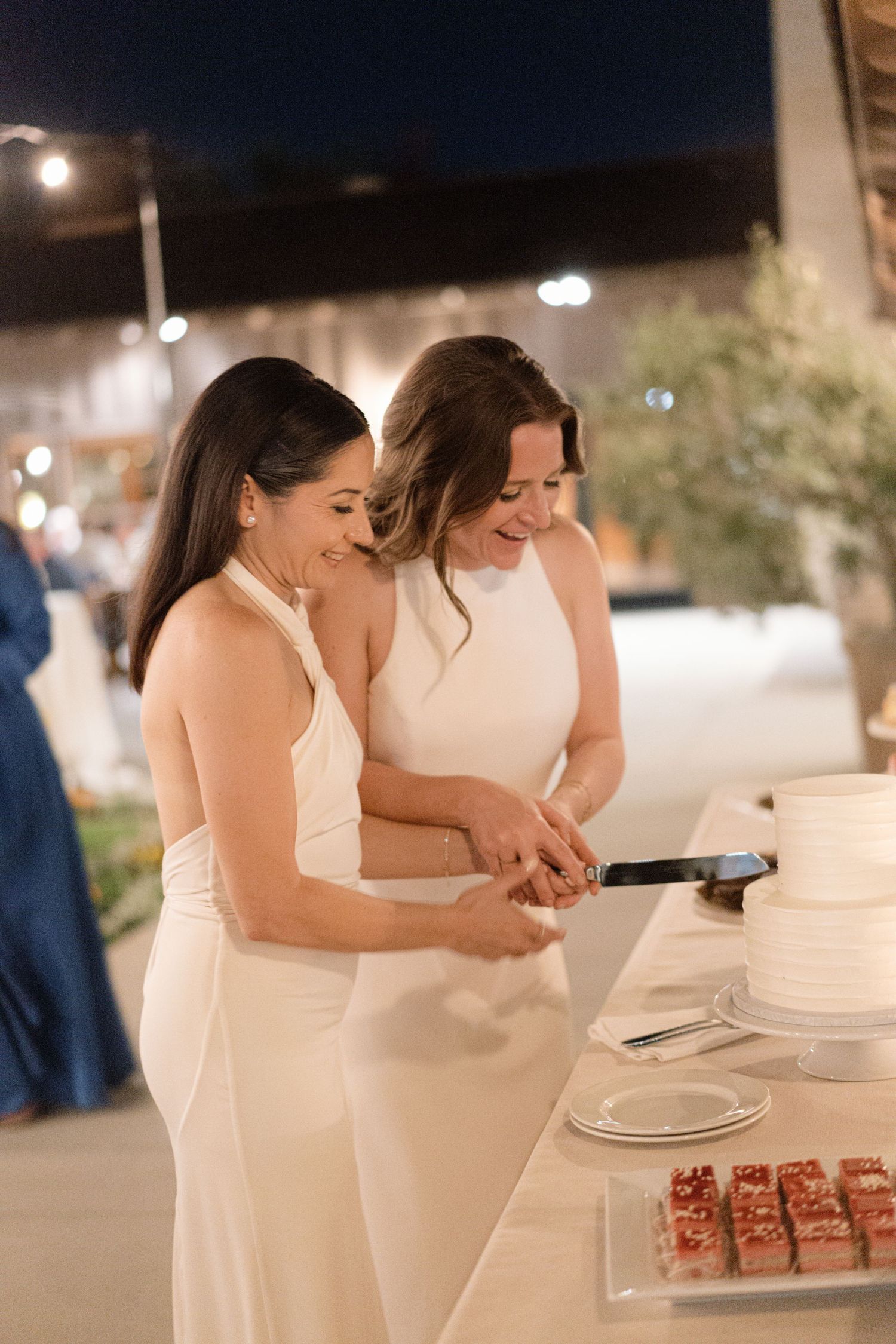 Wedding reception dessert table with white-clothed guests serving cake at night.