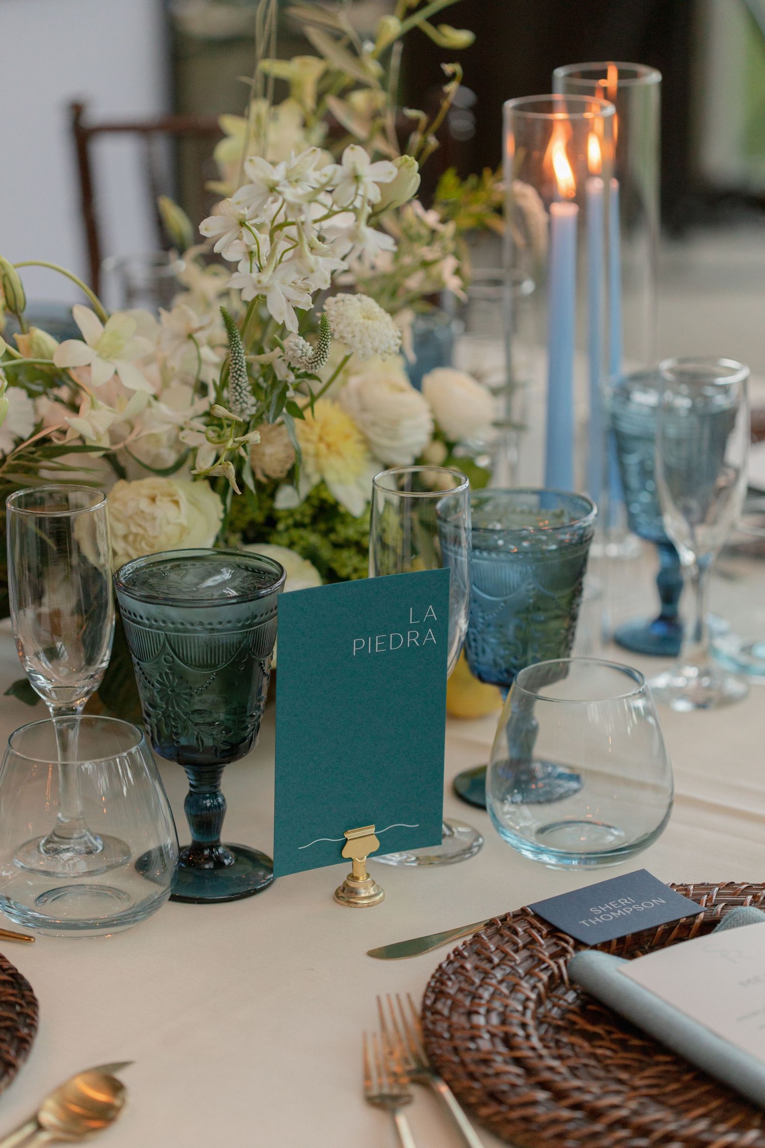 Elegant table setting with blue glassware, white flowers and a teal menu book.