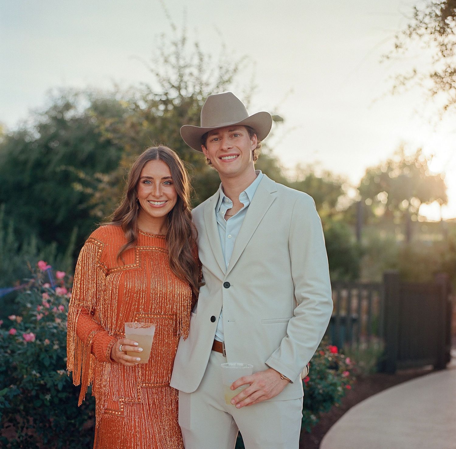 Stylish couple at sunset with western-inspired attire in a garden setting.