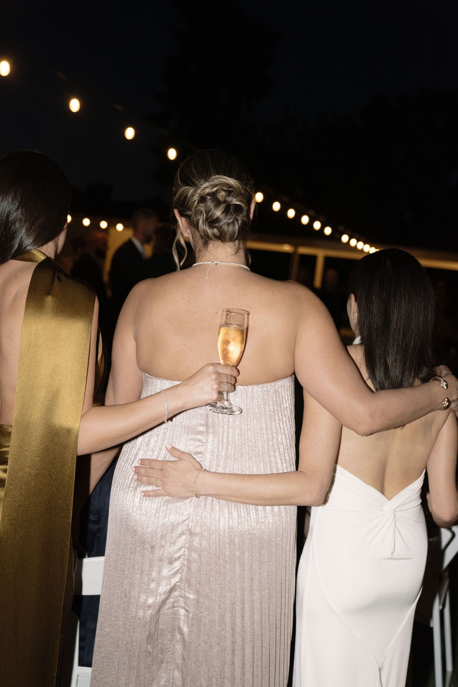 Wedding guests in formal attire holding champagne glasses at outdoor evening reception.