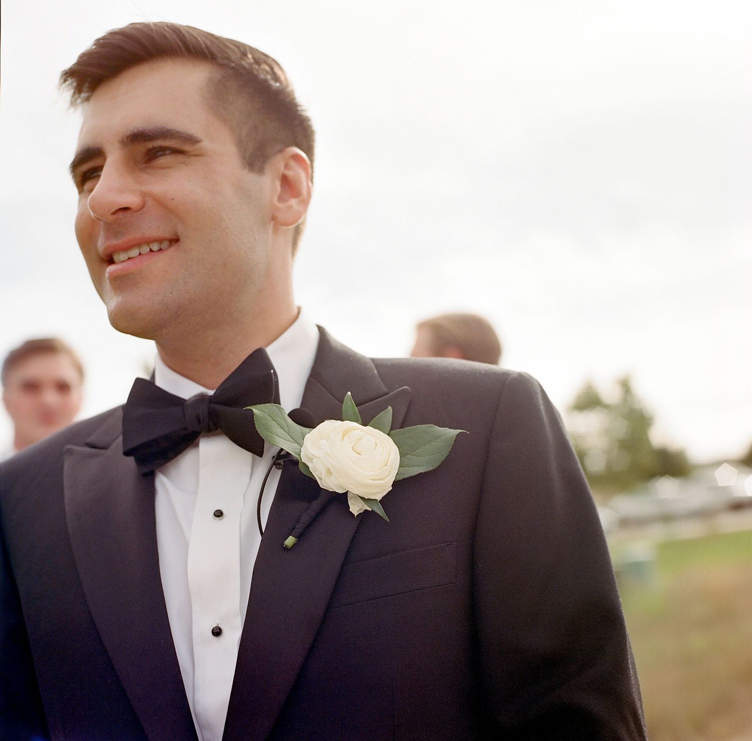 A formal wedding attire with a black tuxedo, bow tie and white rose boutonniere.