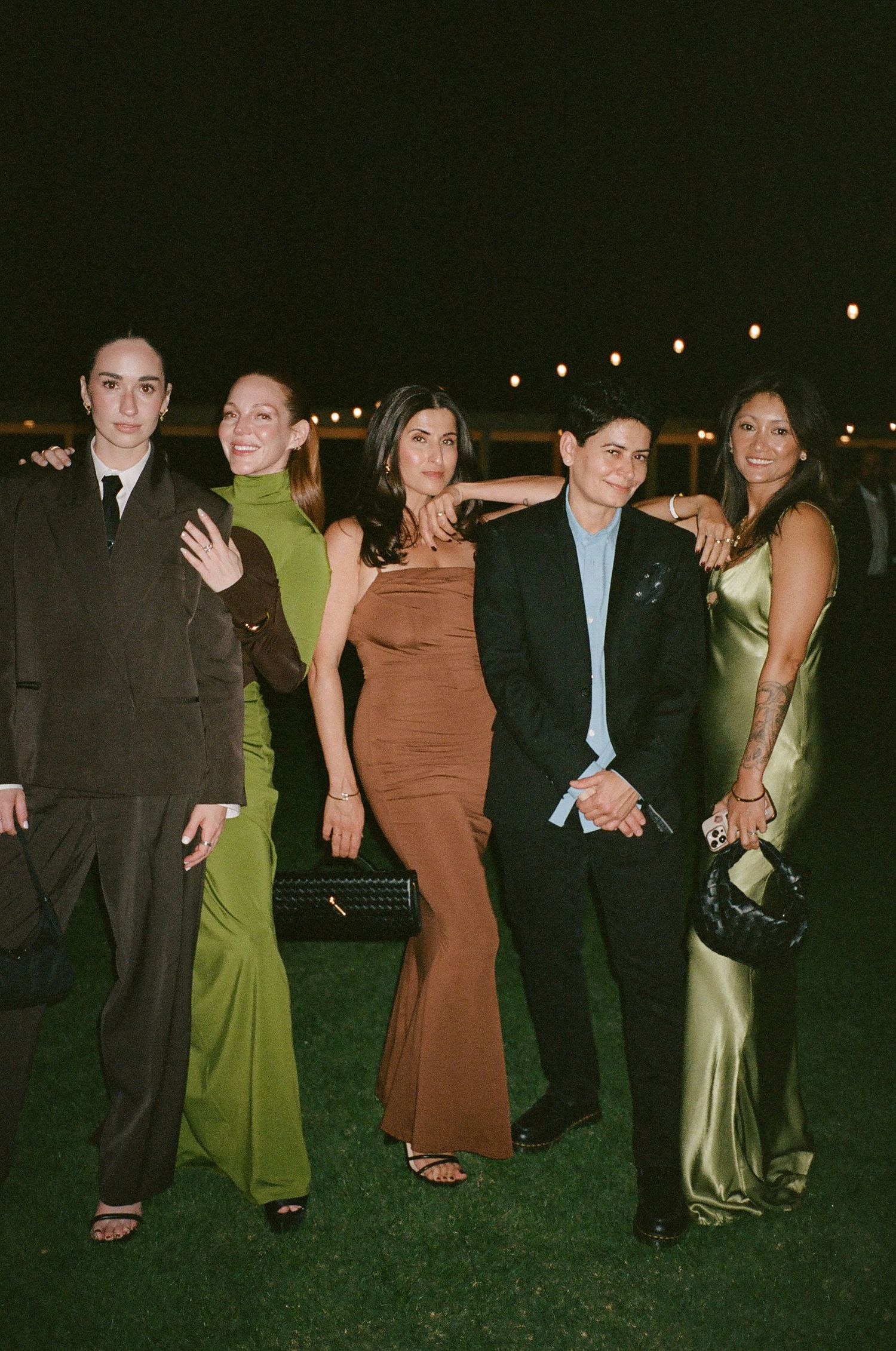 Group photo of wedding guests in formal attire standing together on grass at night.