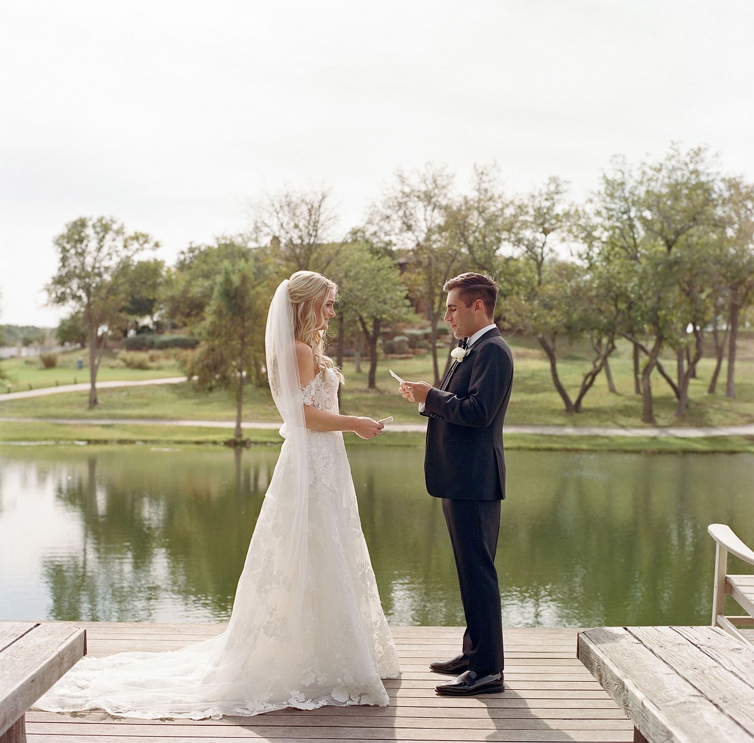 Newlyweds sharing a romantic moment on a lakeside dock during their wedding day.
