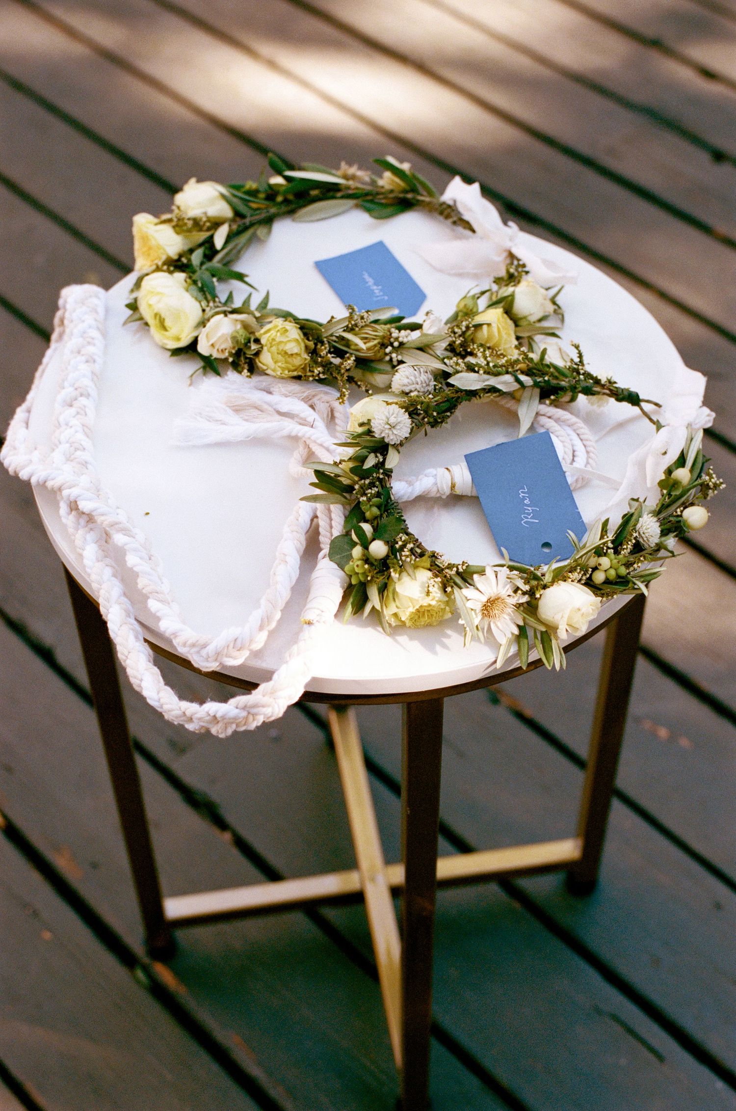 White floral crowns adorned with greenery displayed on wooden stools.