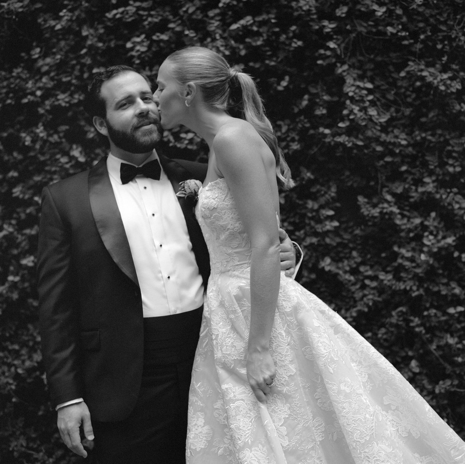 Romantic black and white wedding photos showing tender moments between newlyweds against a leafy backdrop.