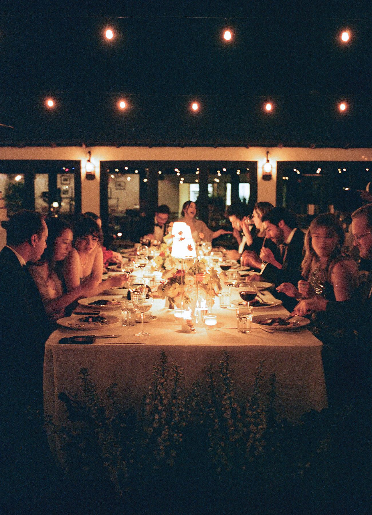 Elegant candlelit dinner reception with string lights and guests seated at long tables.