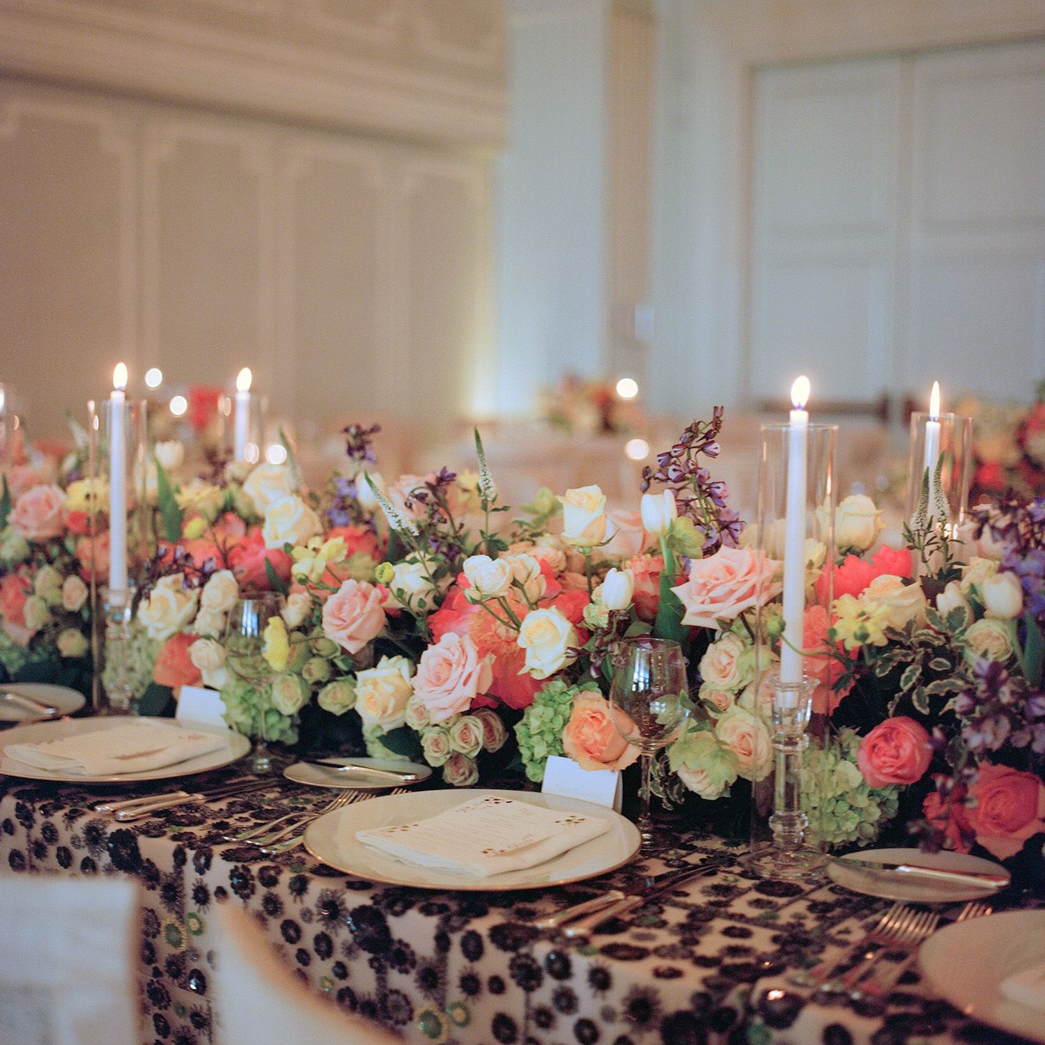 Elegant wedding reception table with floral centerpieces, candles and patterned linens.