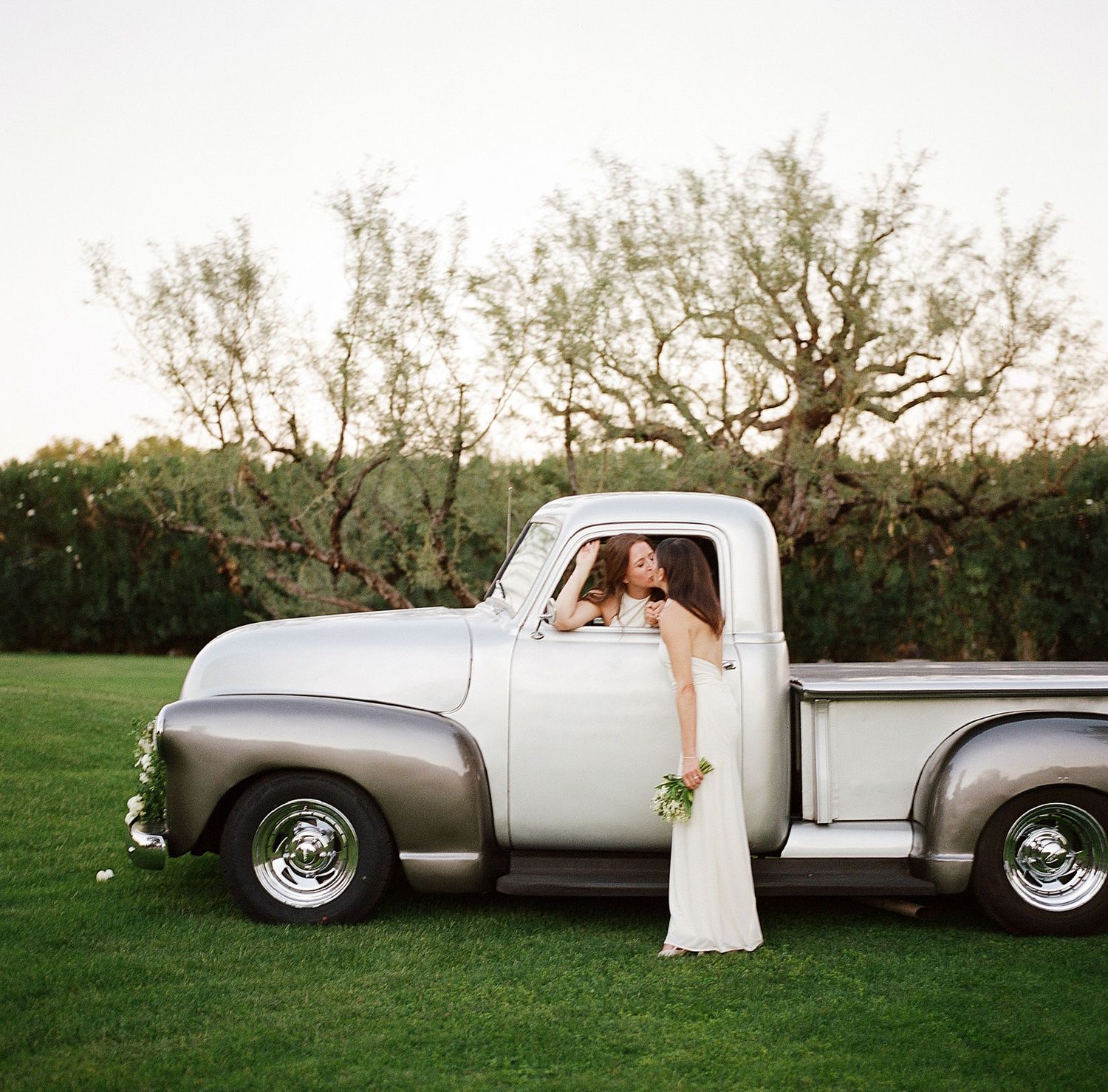A vintage silver pickup truck decorated for a wedding on a grassy lawn.