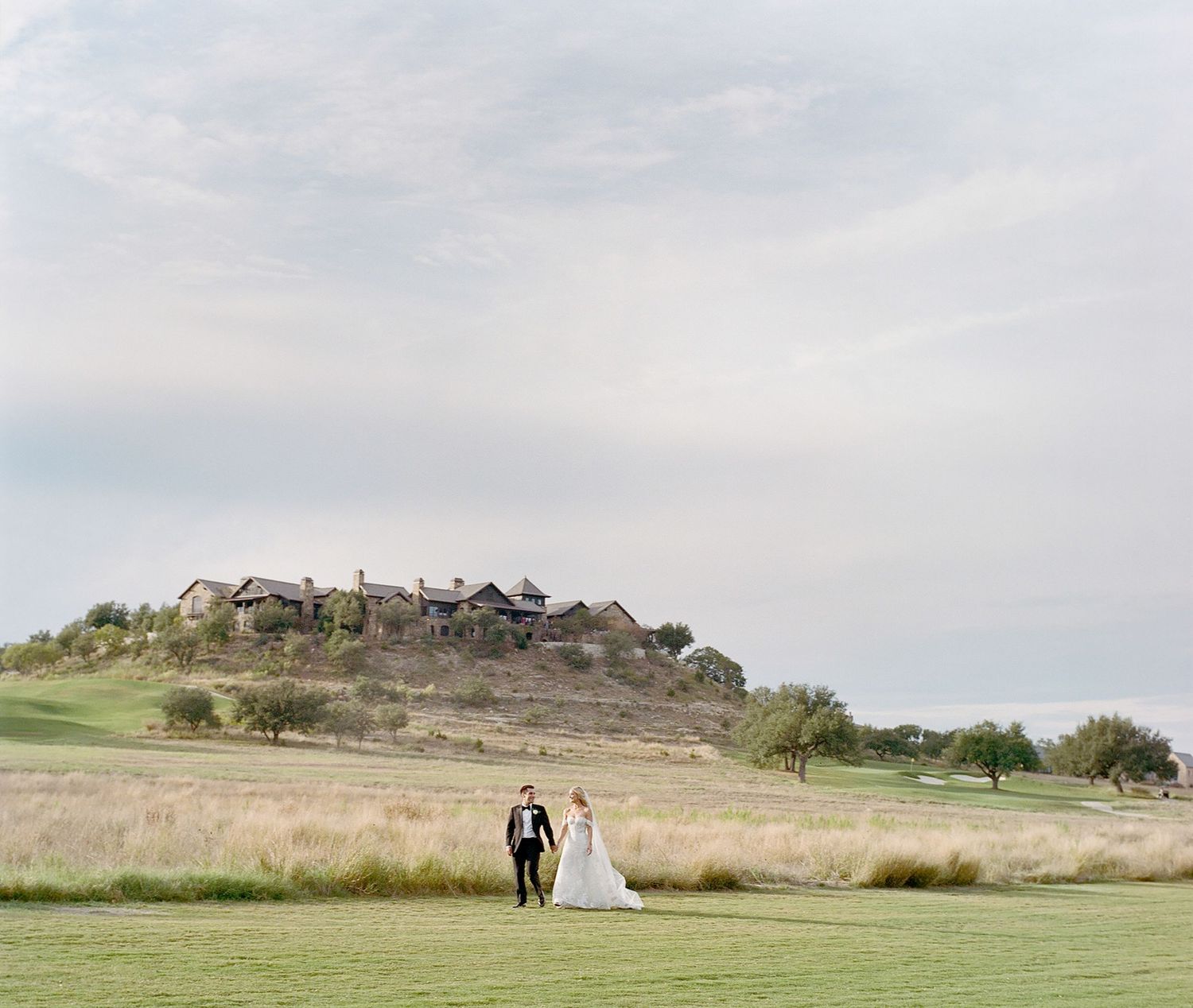 Wedding couple walking together across a scenic hilltop landscape at sunset.