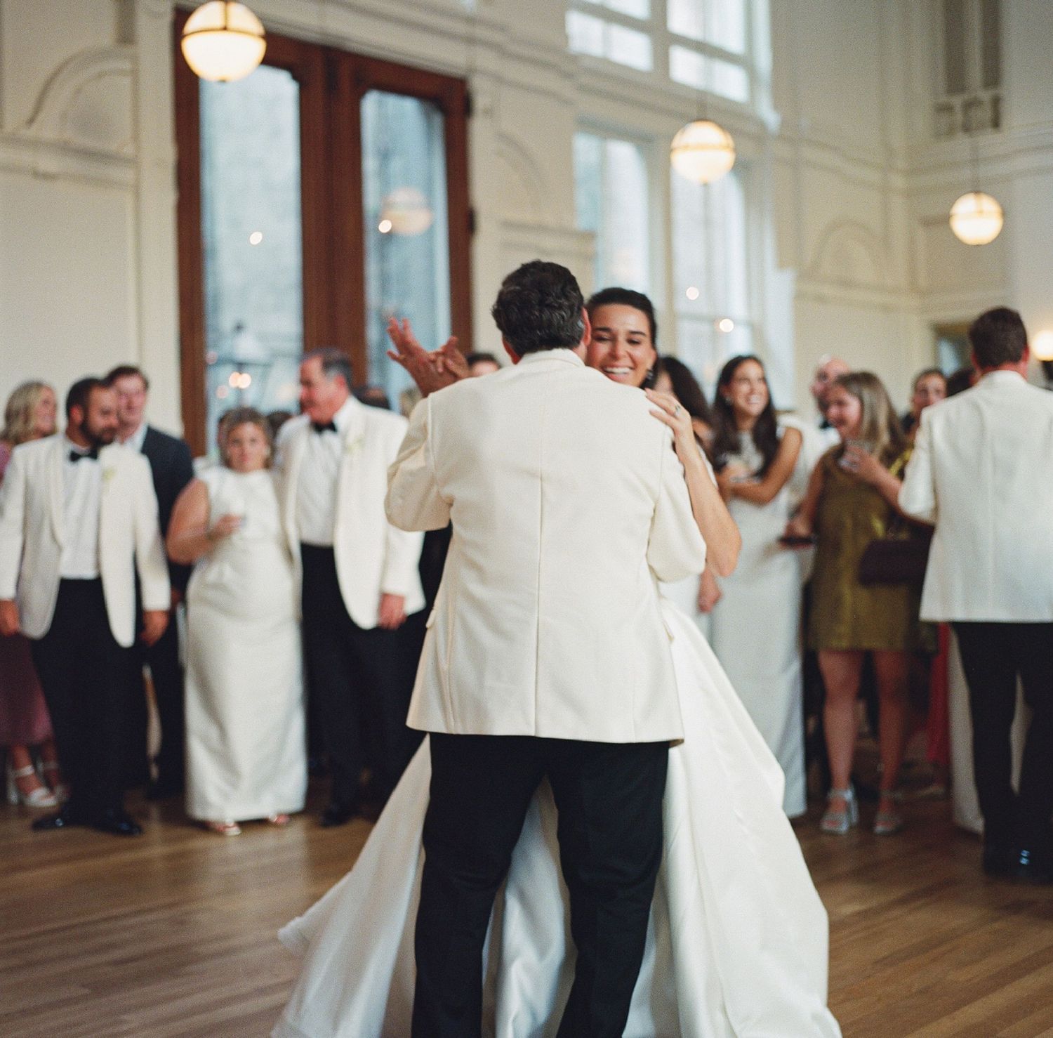 Wedding reception scene in an elegant ballroom with white-clothed tables and warm lighting.