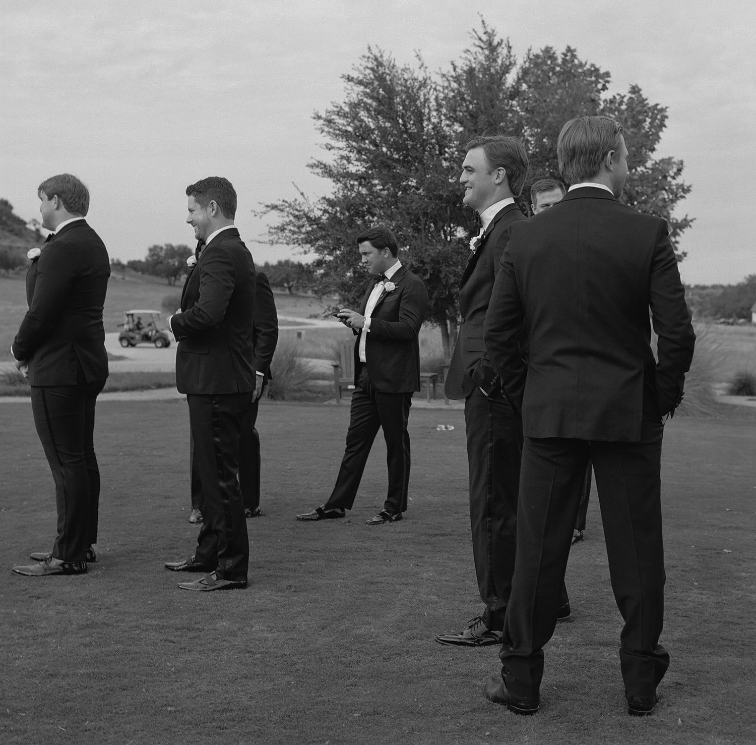 Black and white photo of groomsmen standing in formation on grassy field.