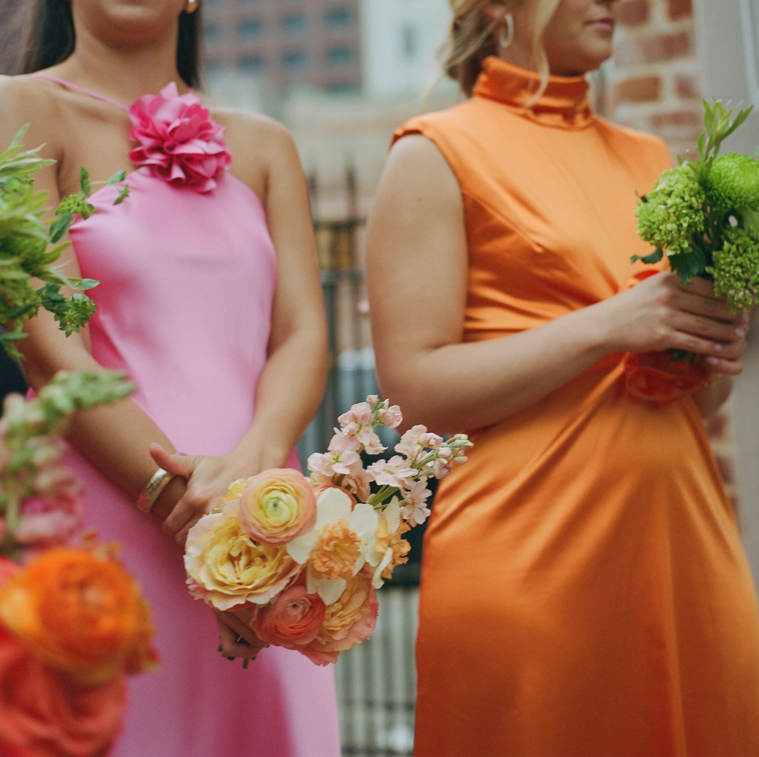 Bridesmaids in pink and orange dresses holding colorful floral bouquets at an outdoor wedding ceremony.