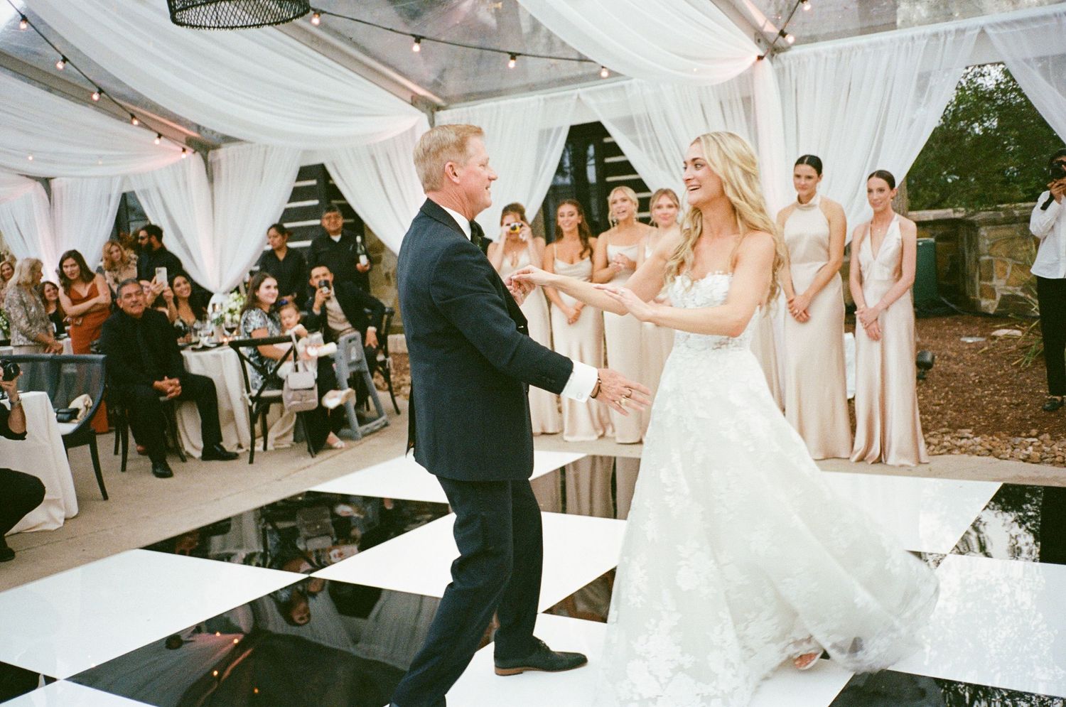 Wedding reception dance floor filled with guests celebrating under white tent decorations.