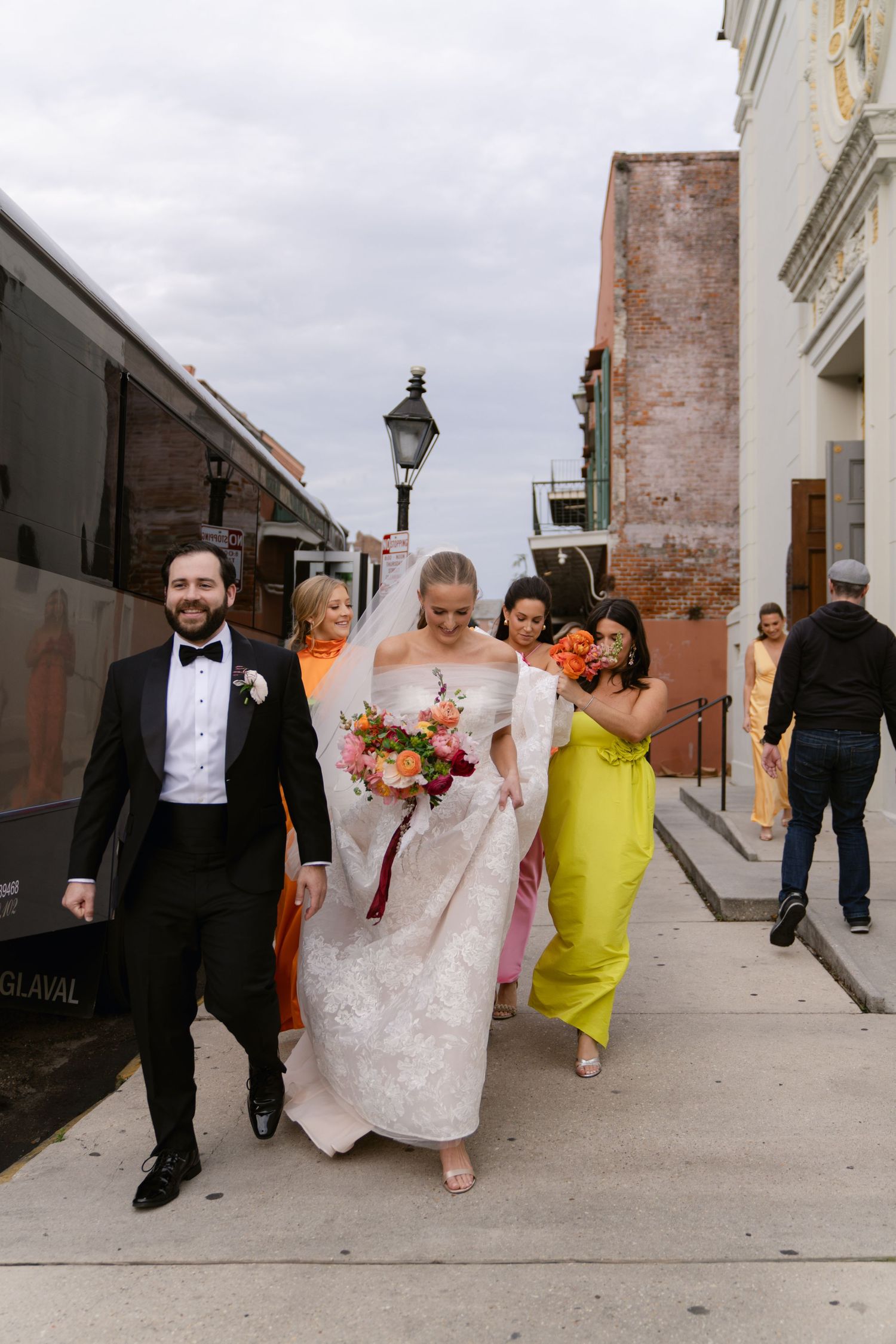 Wedding party walks down historic street with bride in white gown and yellow bridesmaid dress.
