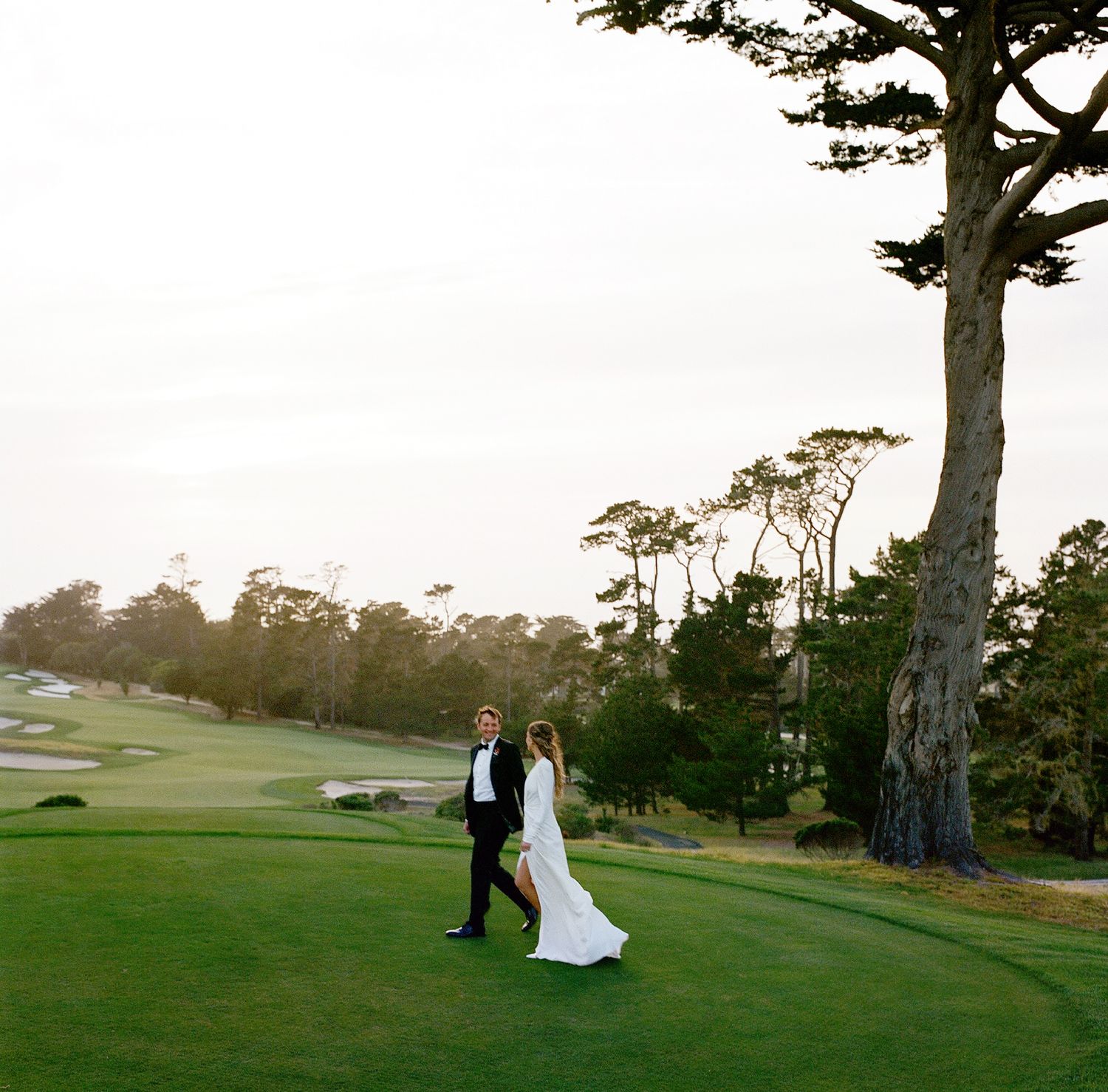 Wedding couple poses on a scenic golf course with trees at sunset.
