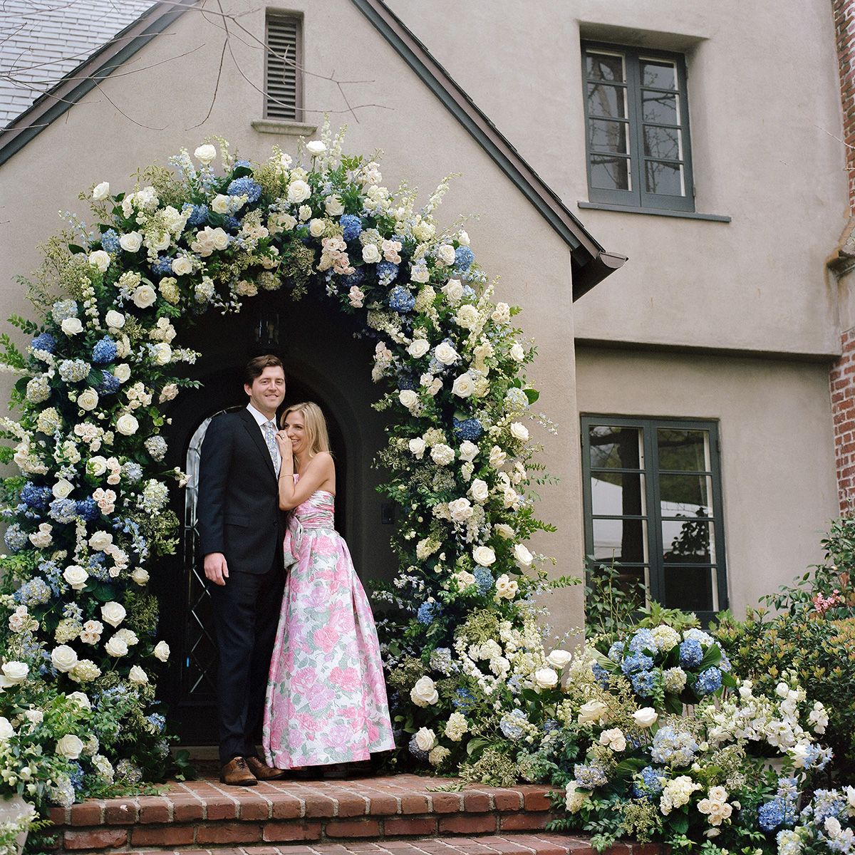 Wedding couple posing under a beautiful floral arch with white and blue roses.