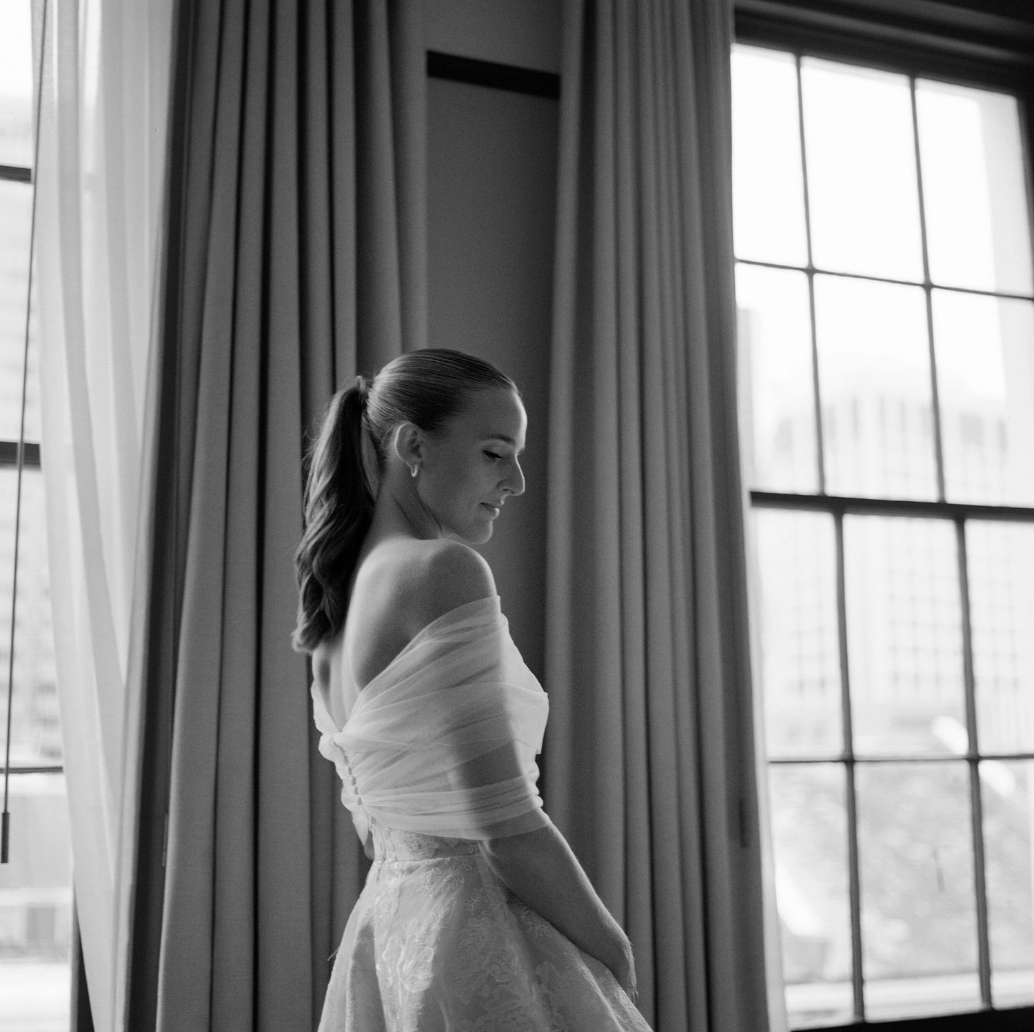 Elegant bridal silhouette against window light in a room with flowing curtains.