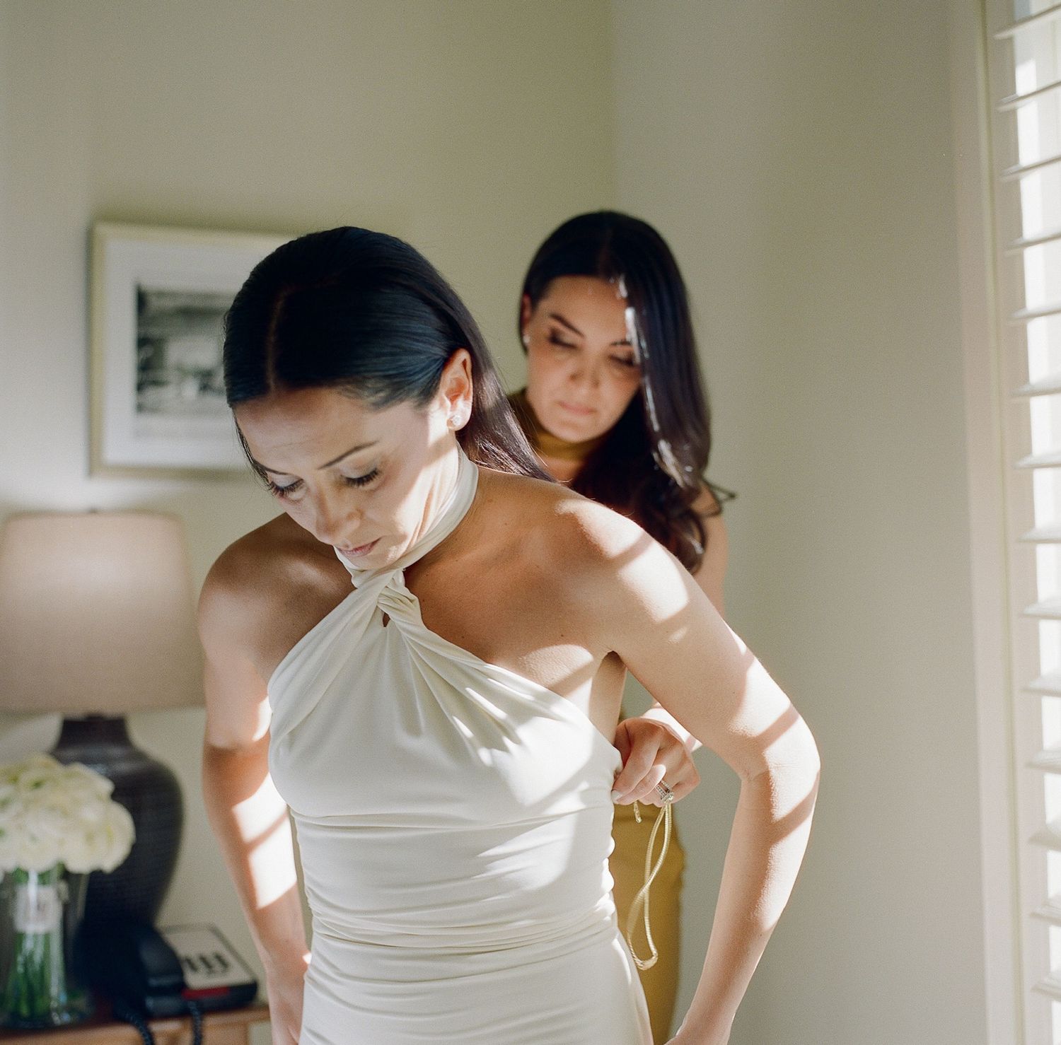 Wedding preparation moment with elegant white dresses in a sunlit room.