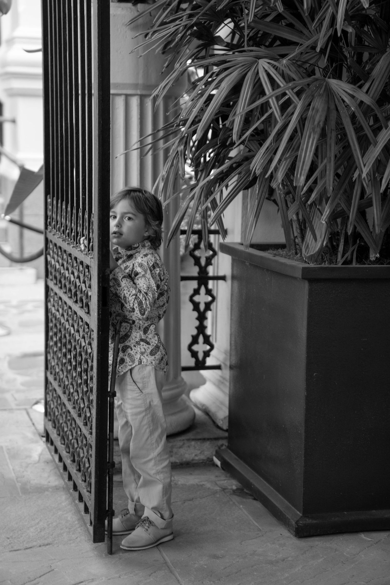A black and white photo of a young attendee standing by an ornate iron gate.