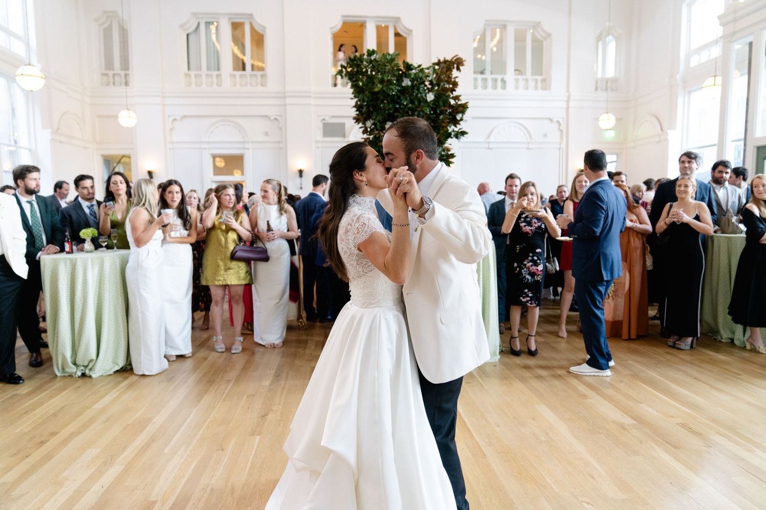 Wedding reception in a grand white ballroom with guests gathered around dance floor.