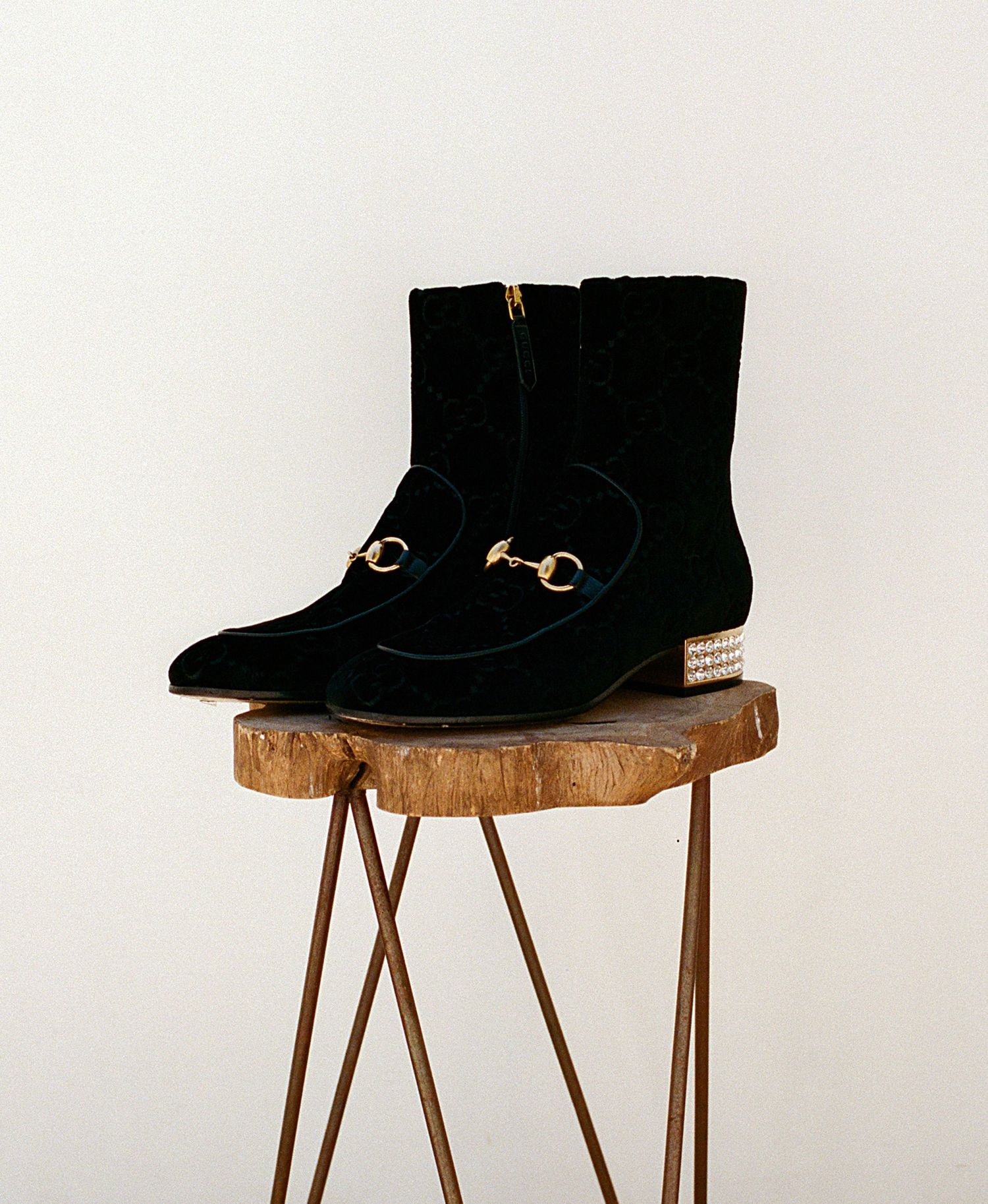 Black suede ankle boots displayed on wooden stands against white background.