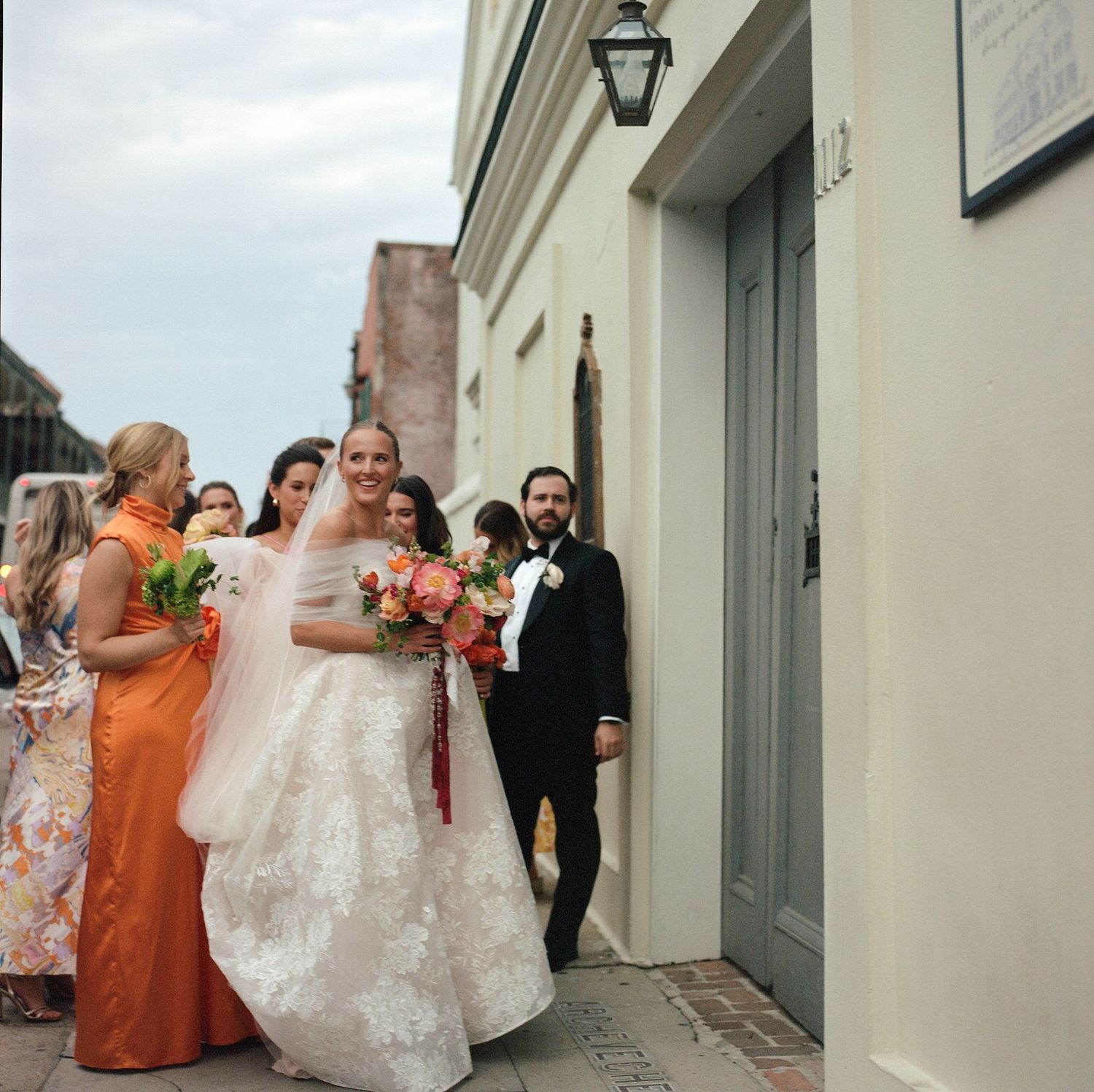 Wedding party members walk along a brick pathway beside a white colonial building.