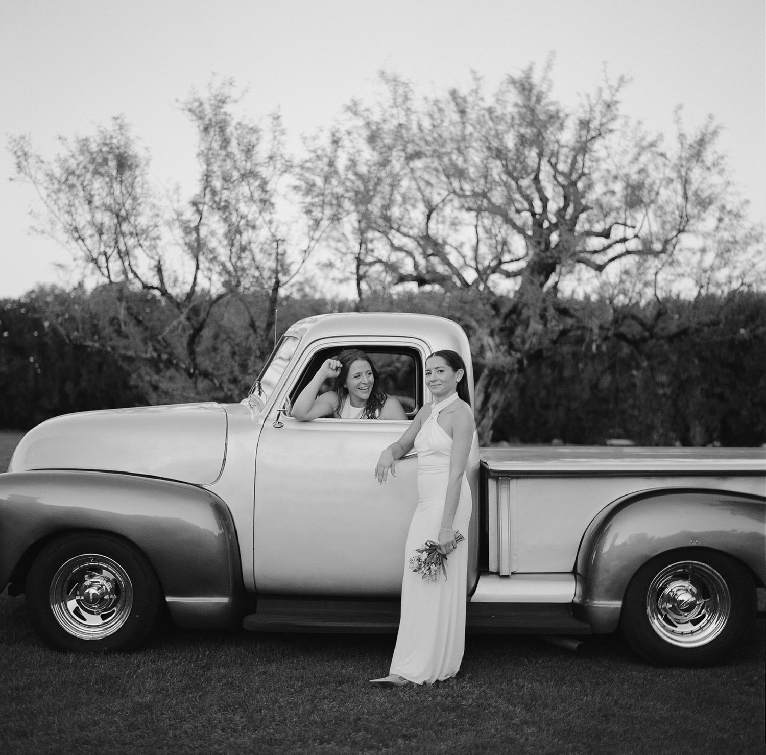 Black and white photo of vintage pickup truck with wedding party at outdoor celebration.