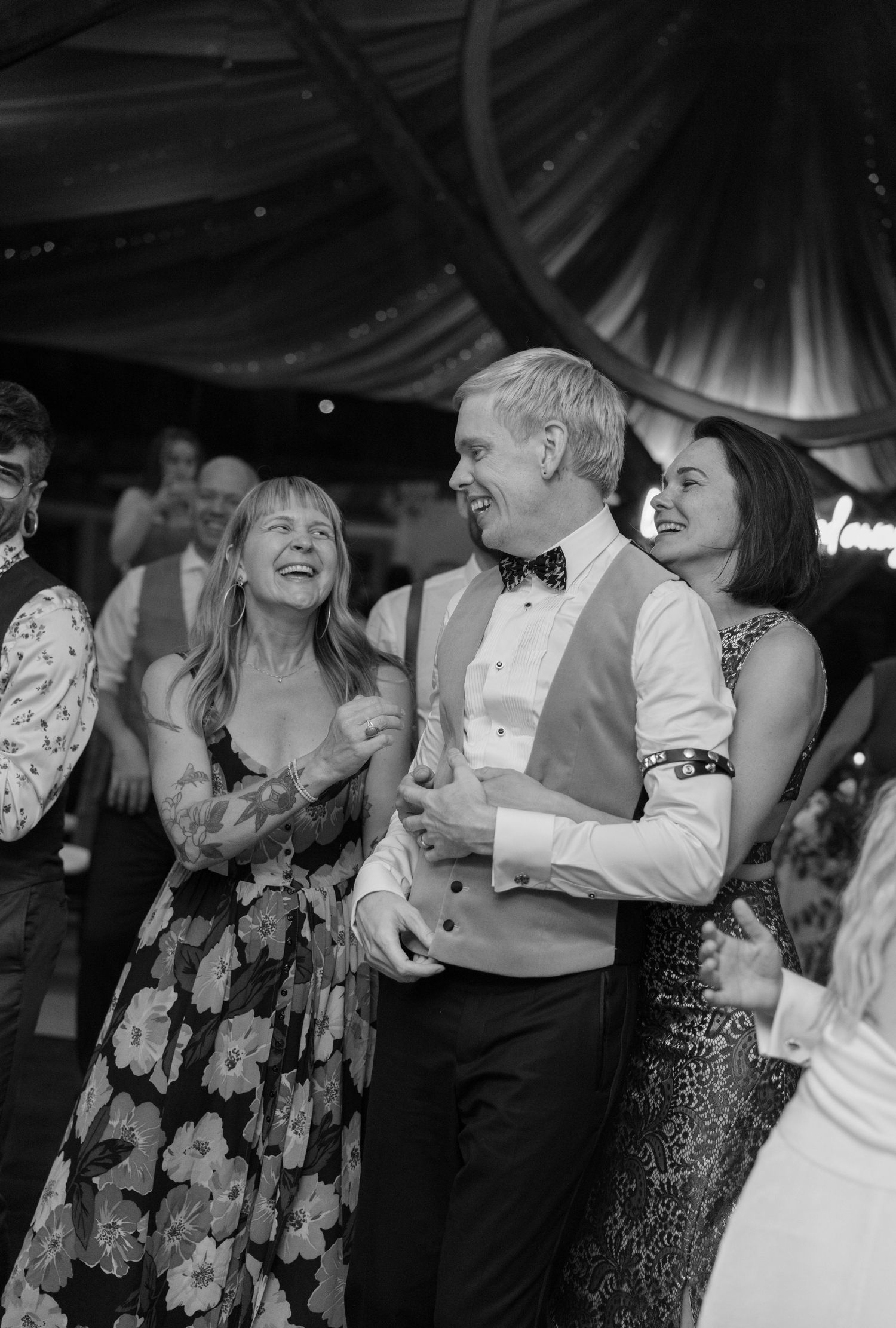 Wedding guests dancing and laughing together under tent lighting at an evening reception.