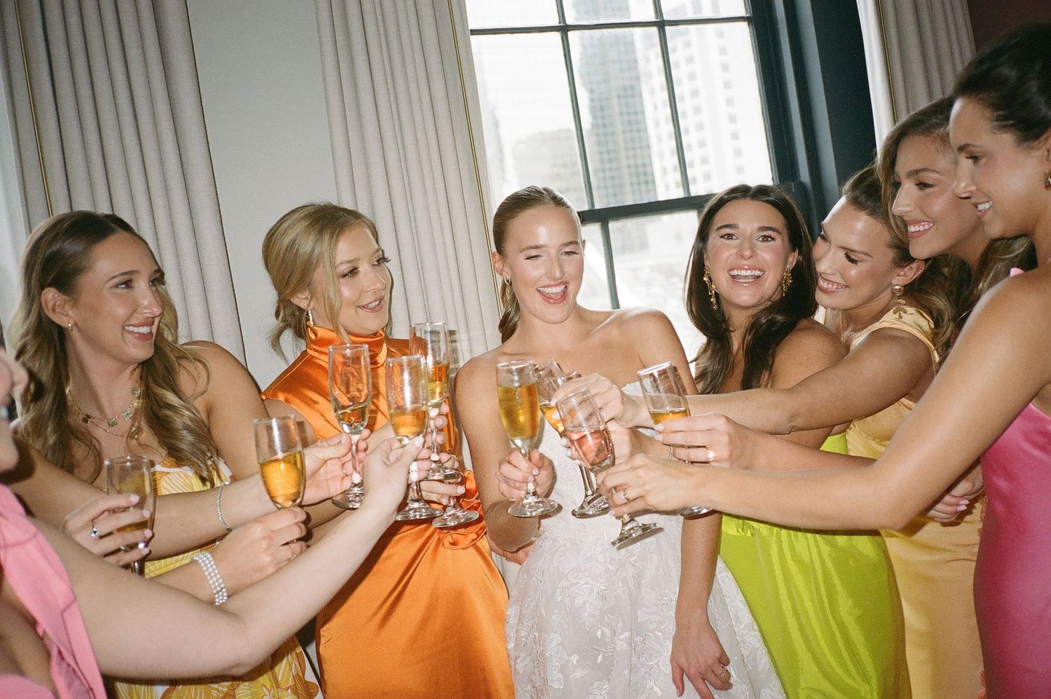 Colorful bridesmaids dresses create a rainbow effect as friends toast together.