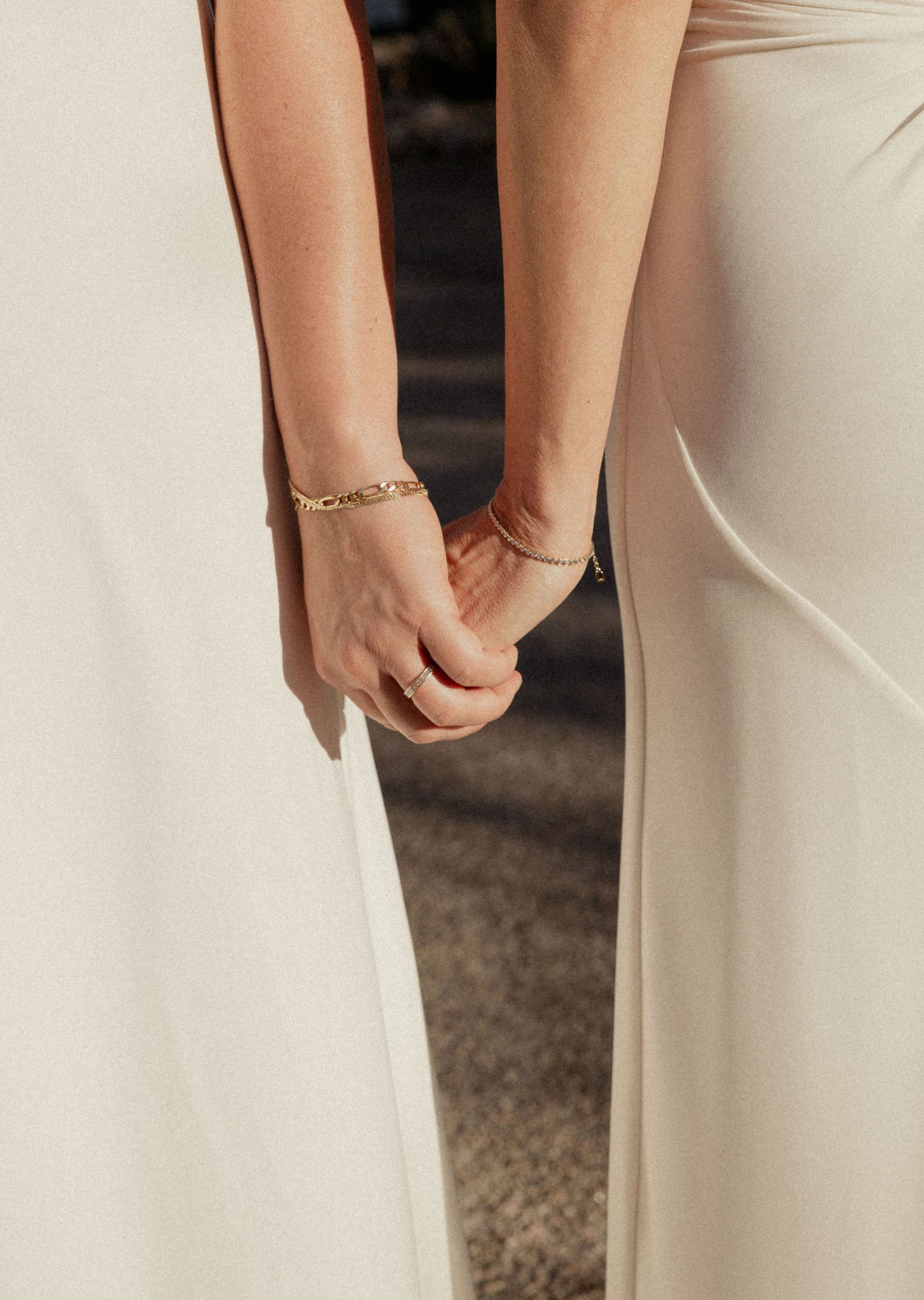 Close-up of hands wearing delicate bracelets against a white dress fabric.