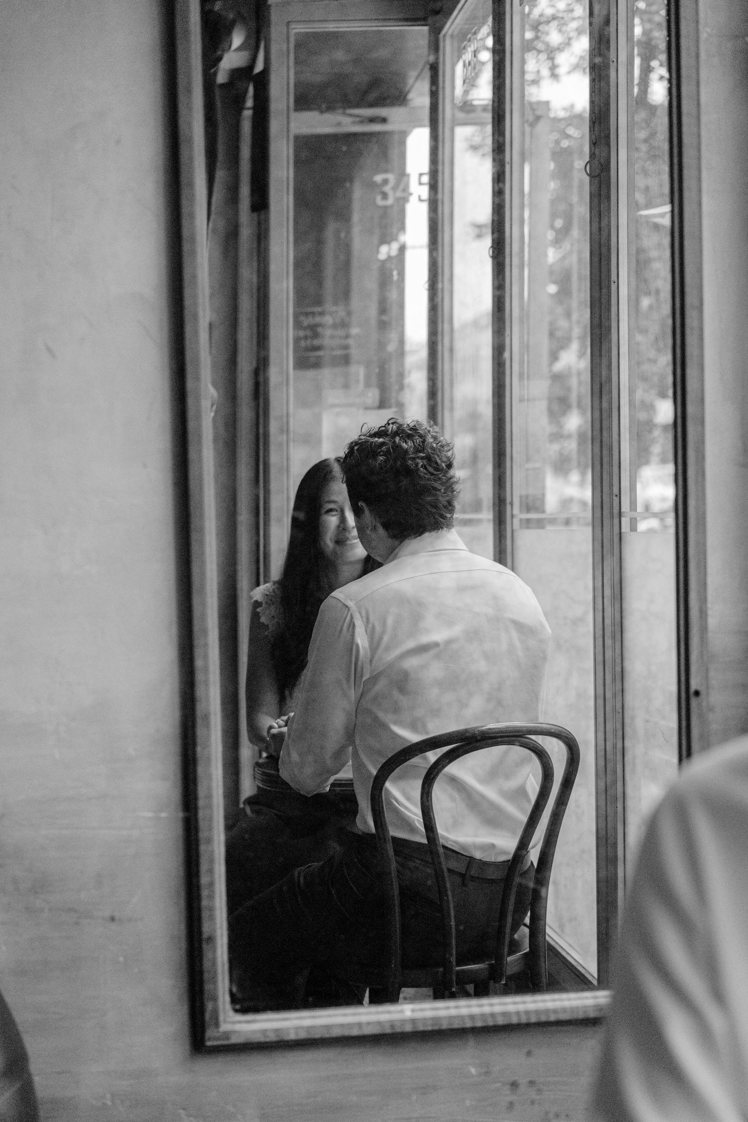 Black and white photo of a couple sharing an intimate moment by a cafe window, reflected in a mirror.