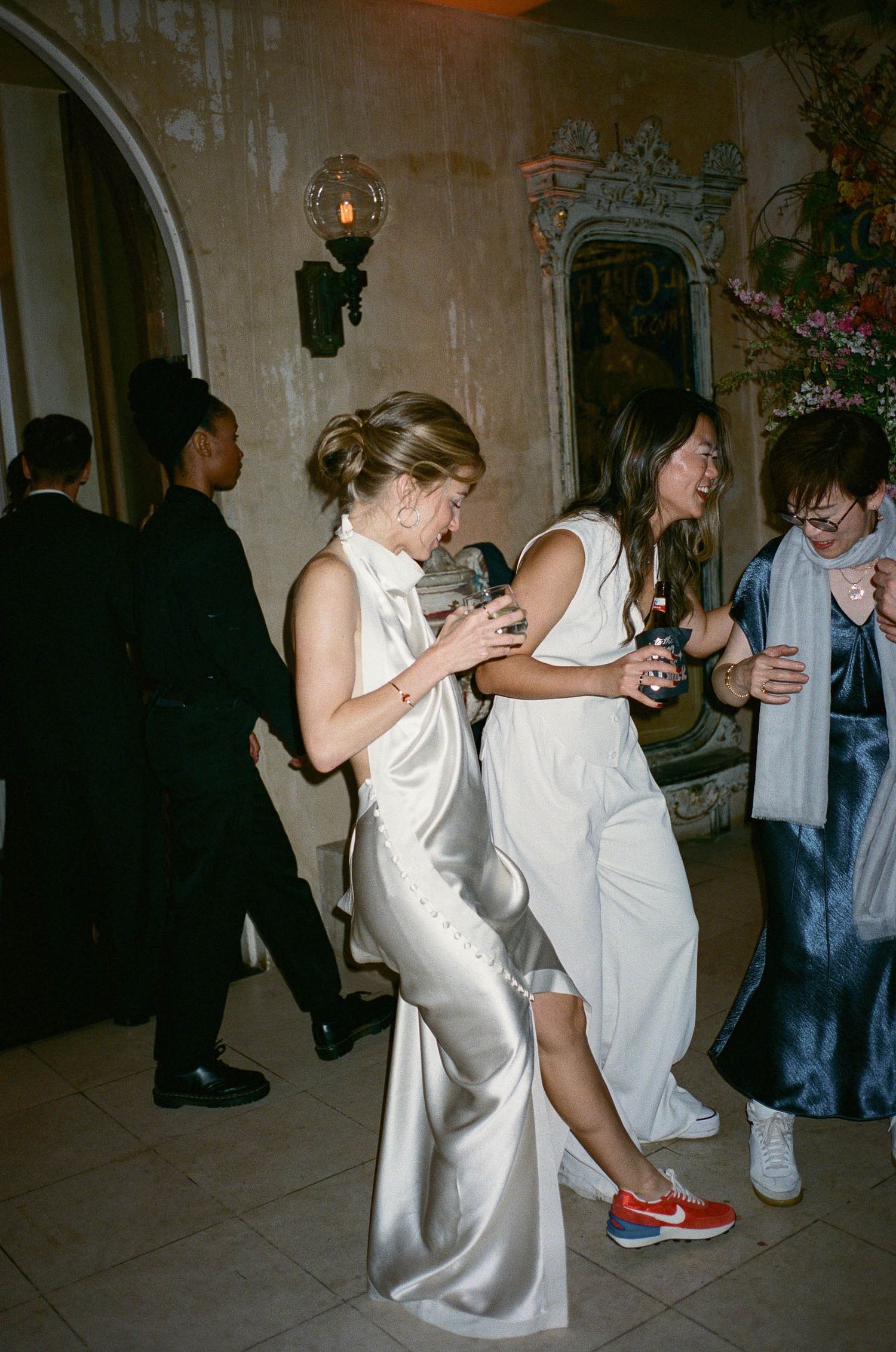 Wedding party members in white dresses dancing energetically on the reception dance floor.