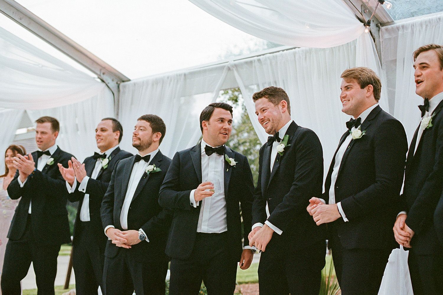 Groomsmen in black suits and ties lined up for a formal wedding photo.