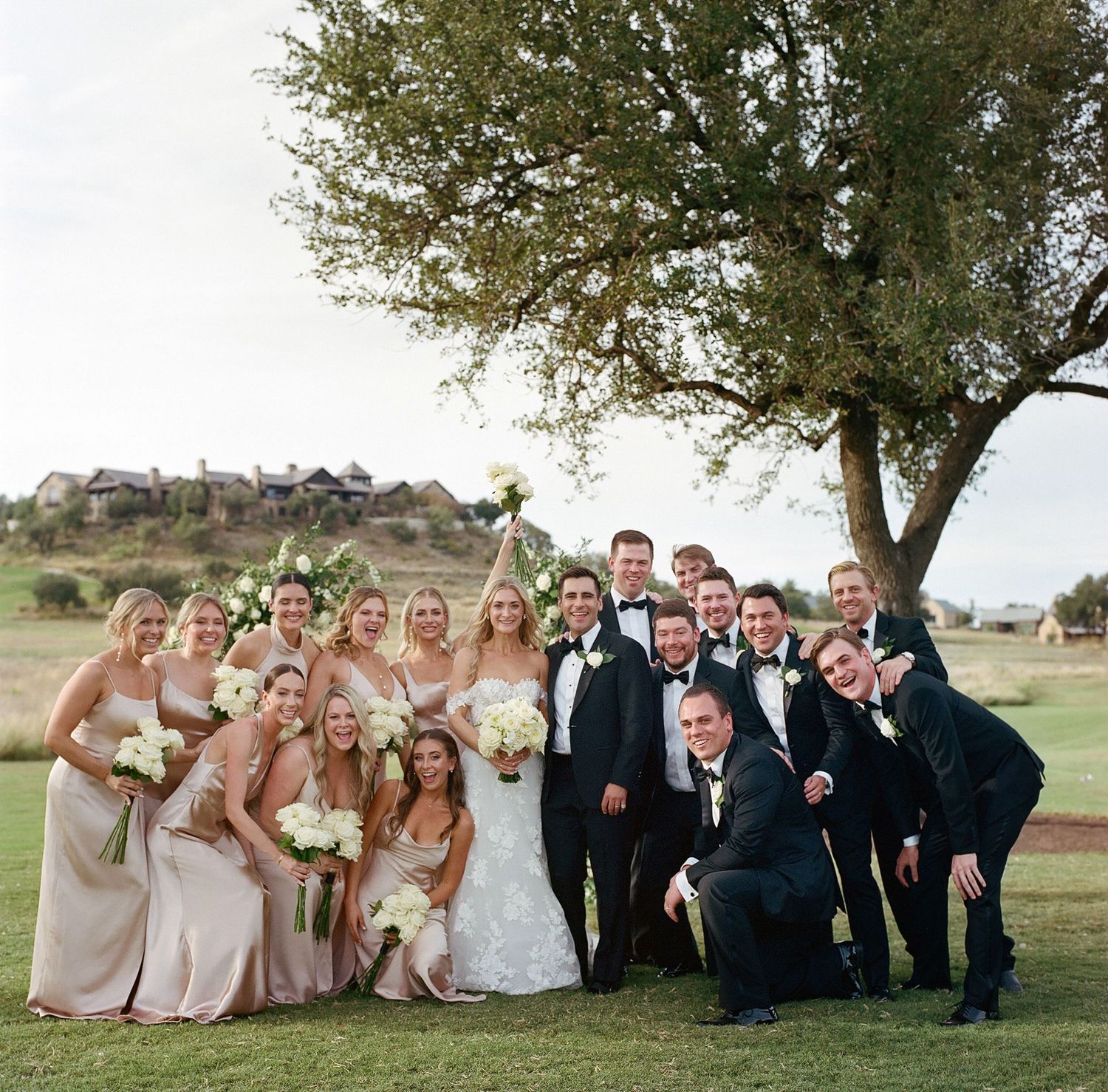 Wedding party in blush pink and black attire posing under a tree.