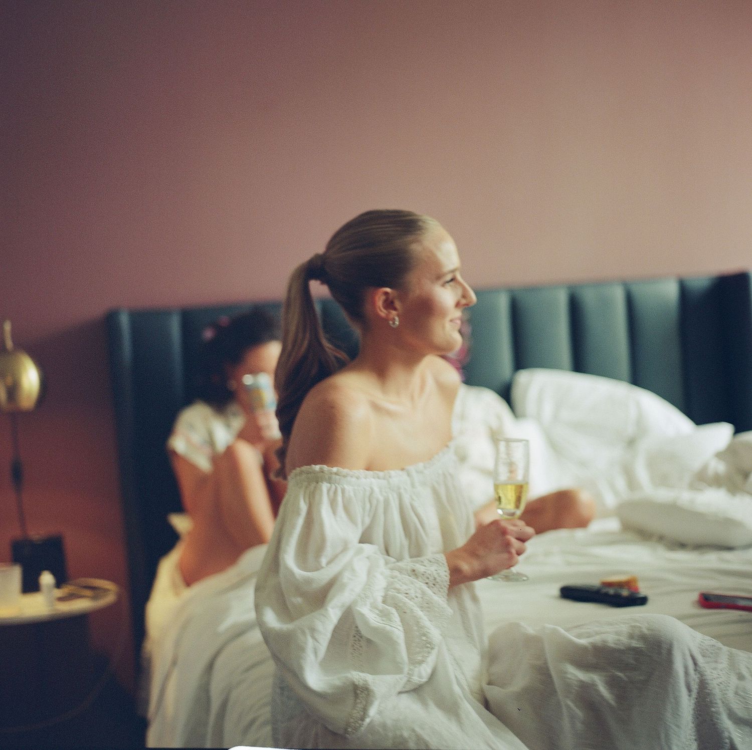 Candid moment of wedding preparation showing woman in white robe holding champagne.