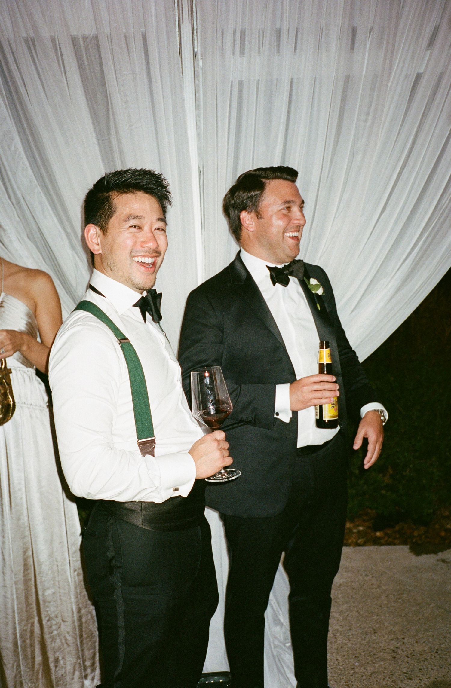 Groomsmen in formal attire laughing and enjoying drinks at wedding reception.