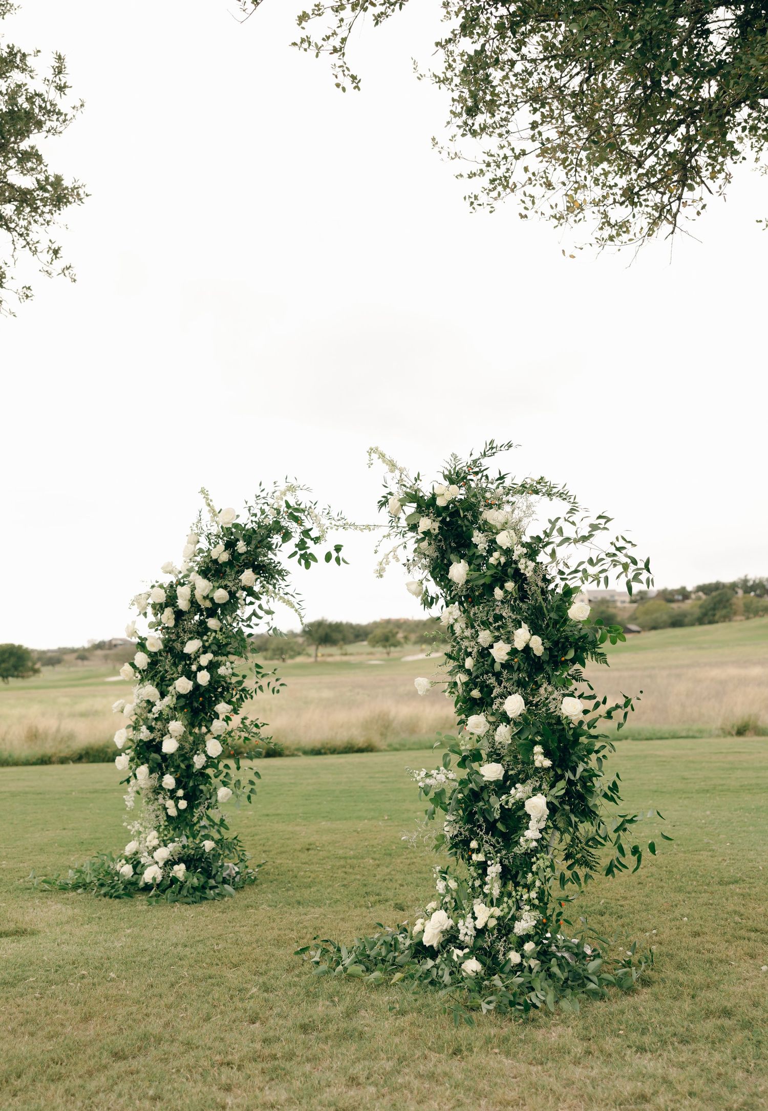 White floral arrangements on stands decorating an outdoor wedding venue.