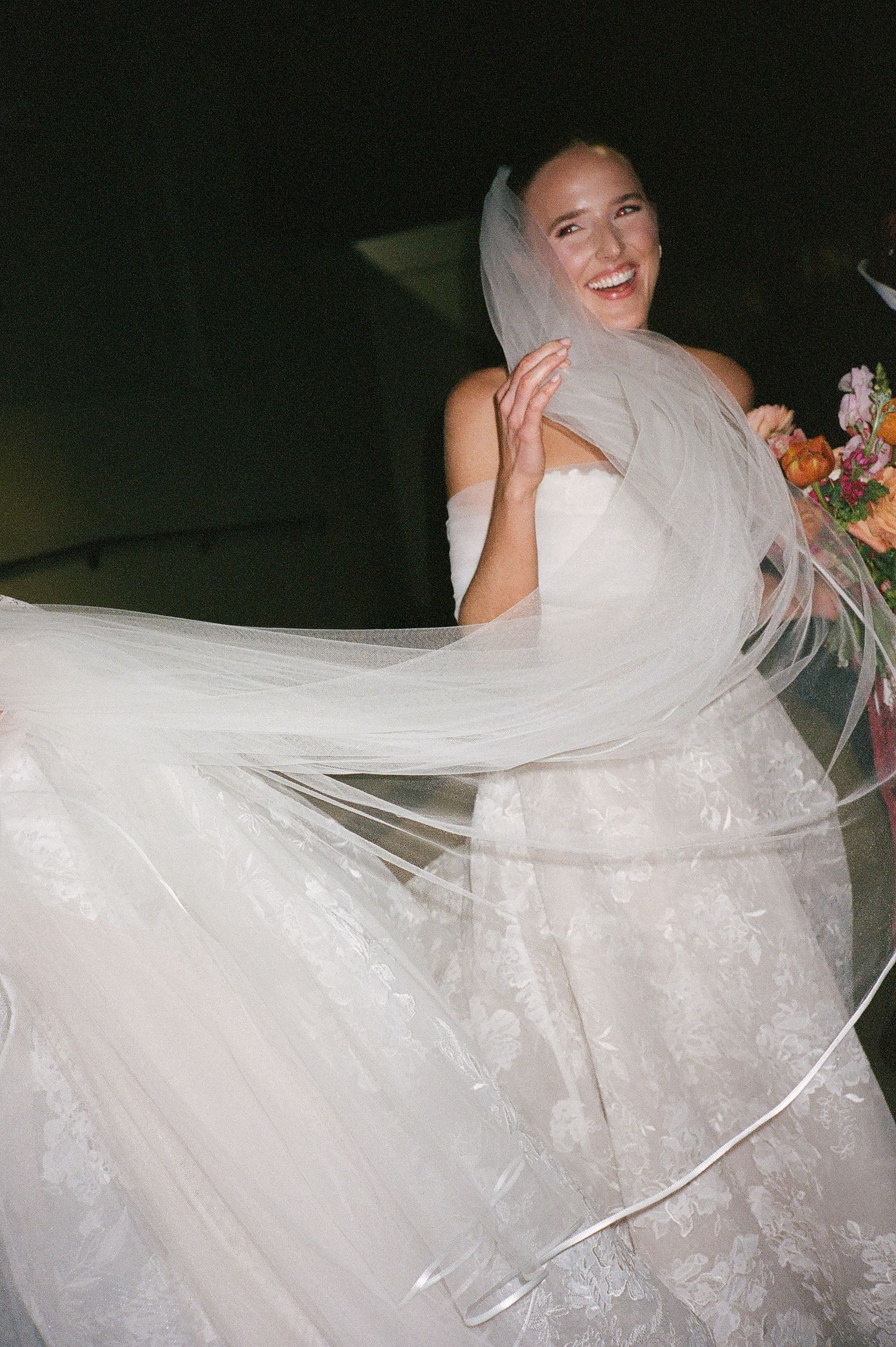 A bride in a lace wedding dress twirls on the dance floor, creating movement with her flowing veil.