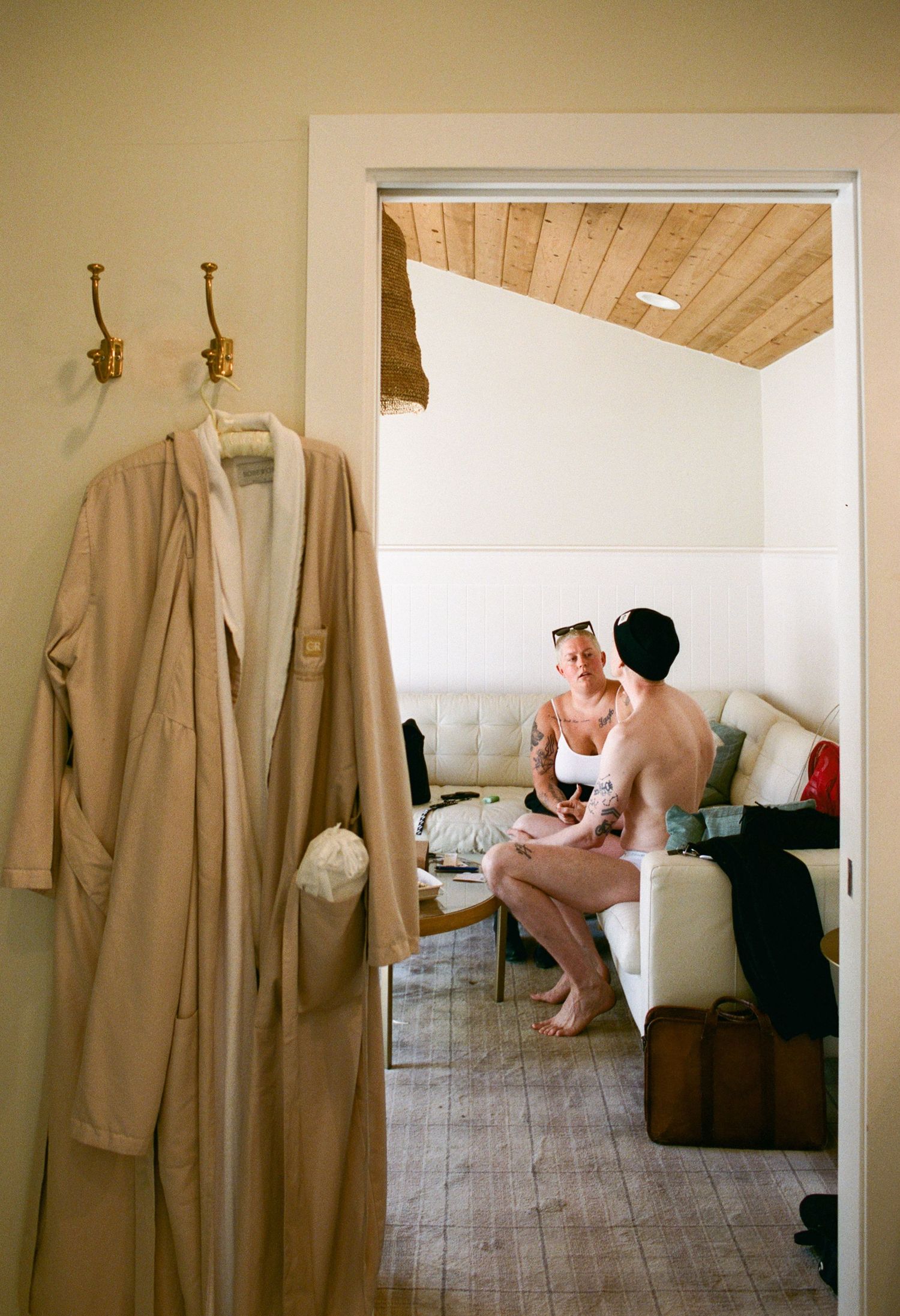 A beige trench coat hangs on display in a minimalist room setting.