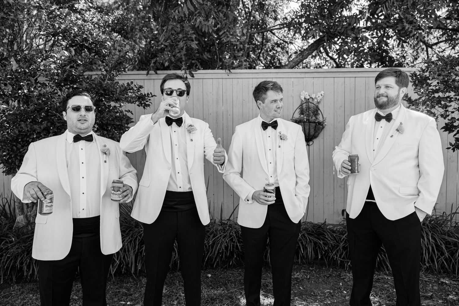 Groomsmen in white dinner jackets and bow ties pose together outdoors in black and white.