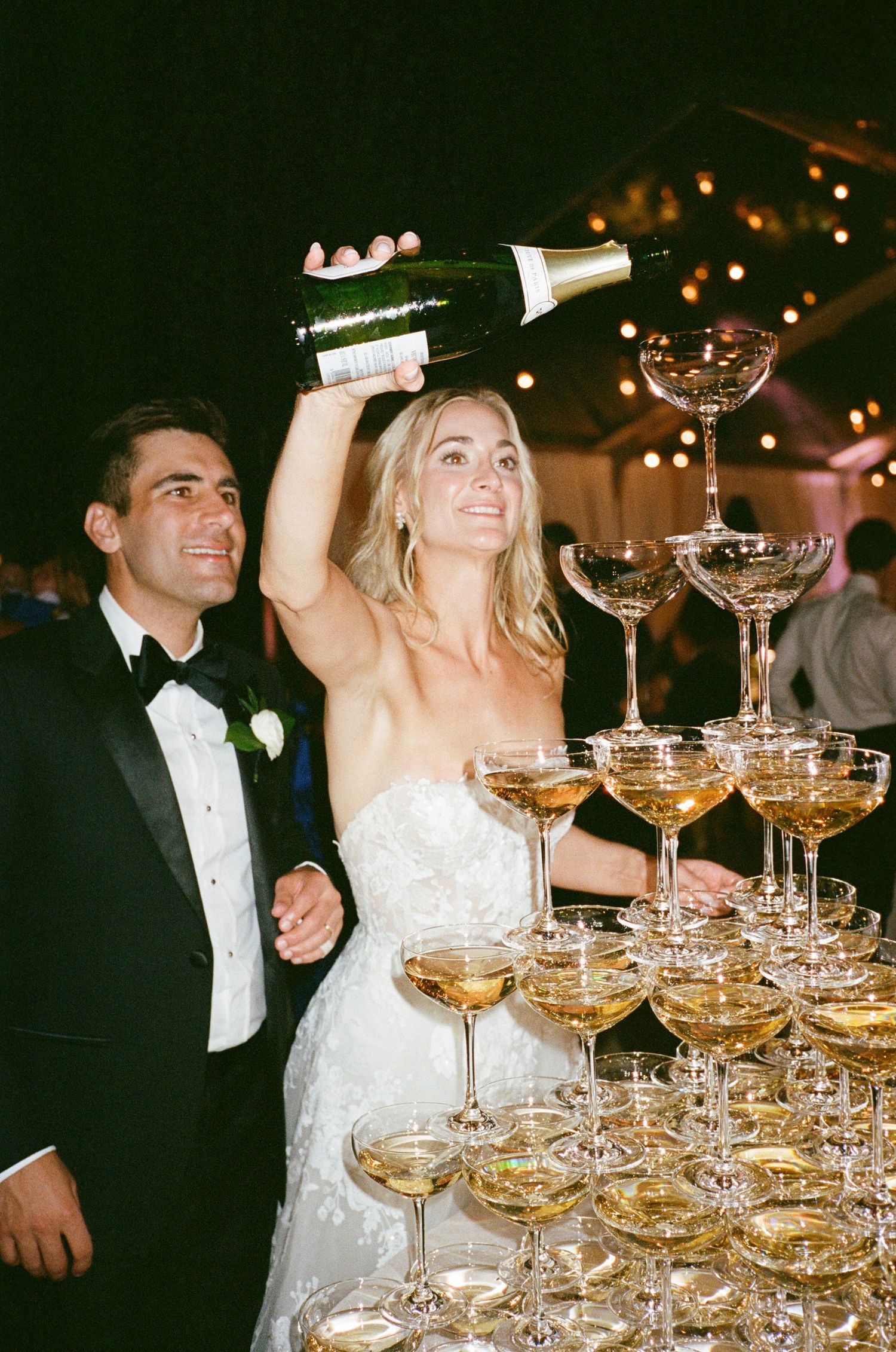 Wedding celebration with champagne tower being poured at an evening reception.