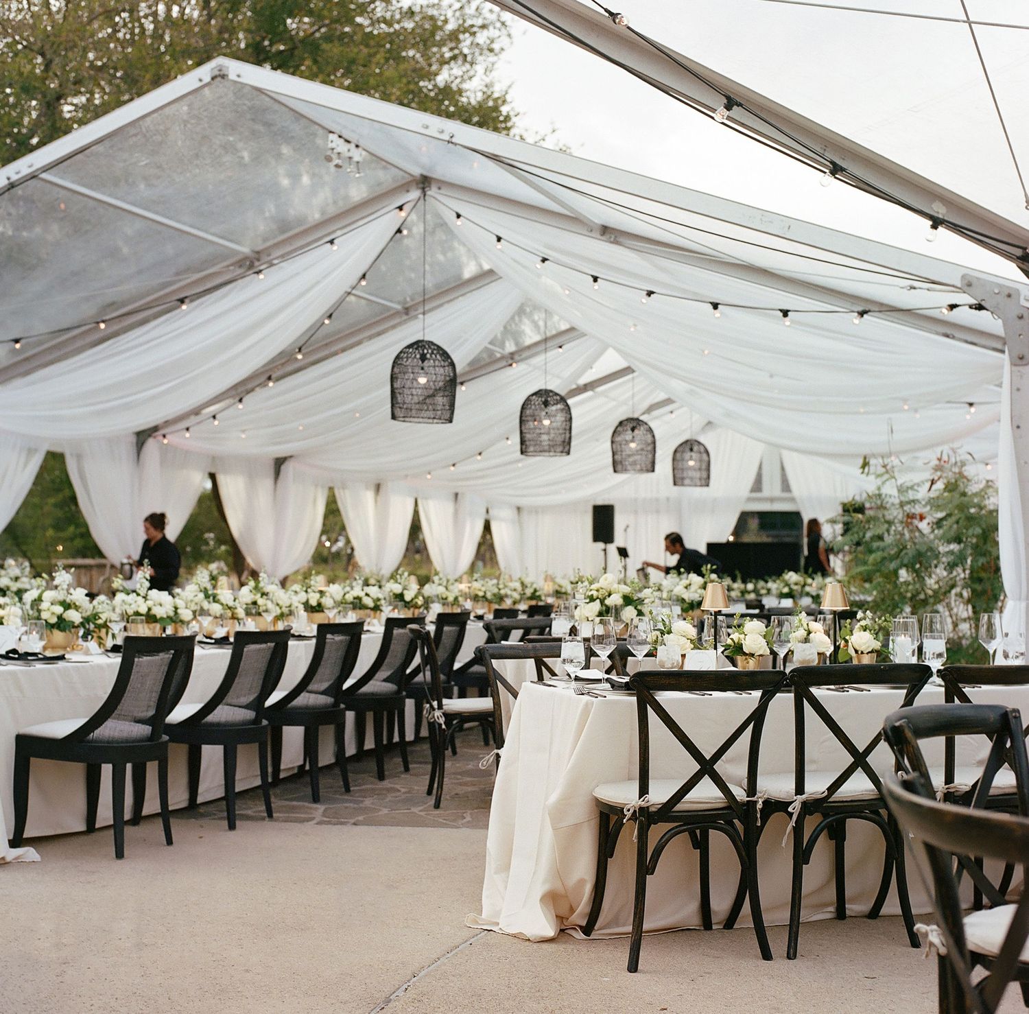 Wedding reception tent with elegant white draping, chandeliers and cross-back chairs.