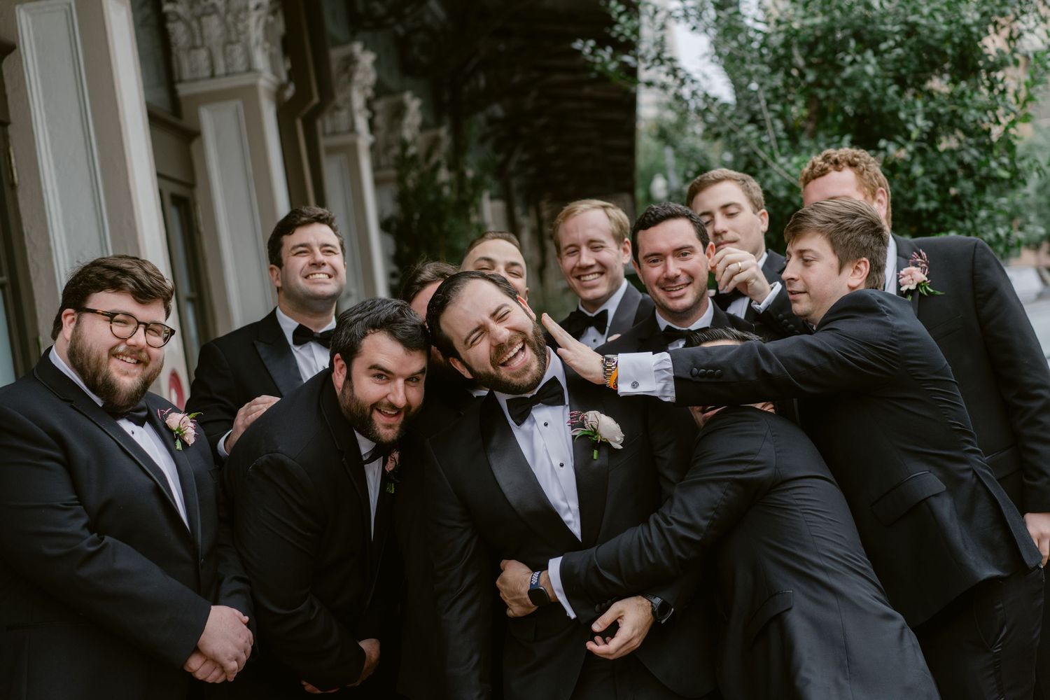 Groomsmen in formal attire posing casually for group photos outdoors.