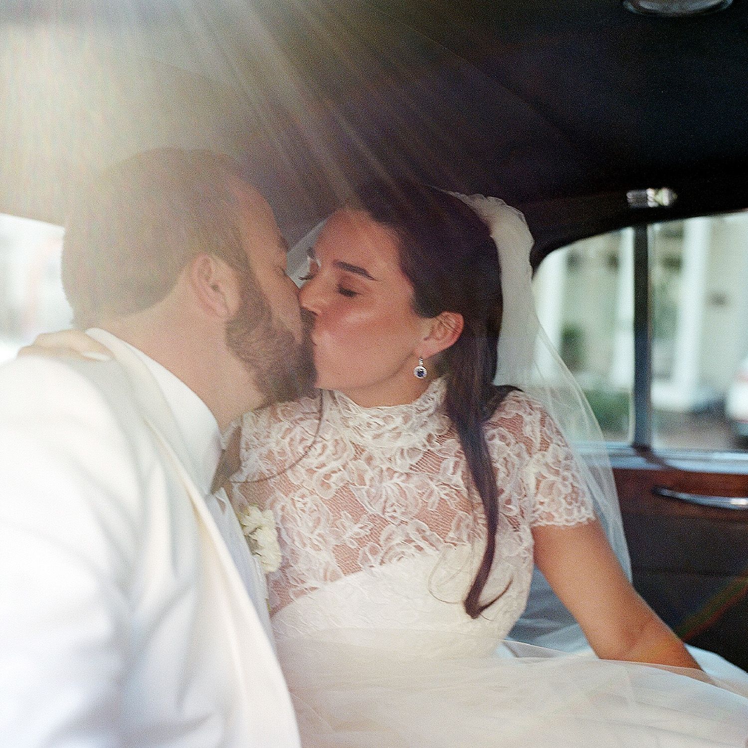 A tender moment shared between a couple in elegant wedding attire inside a car.
